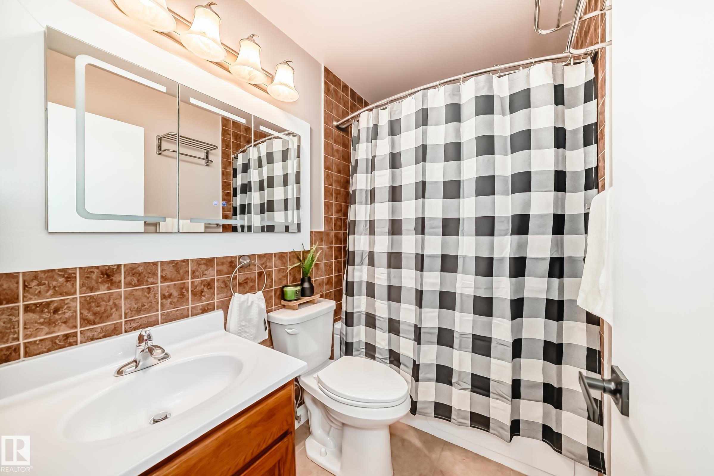 The bathroom features a vanity with a white countertop and a chrome faucet, a wall-mounted mirror with integrated lighting, and a white toilet - 287 Lago Lindo Crescent, Edmonton, AB - Indoor Photo Showing Bathroom