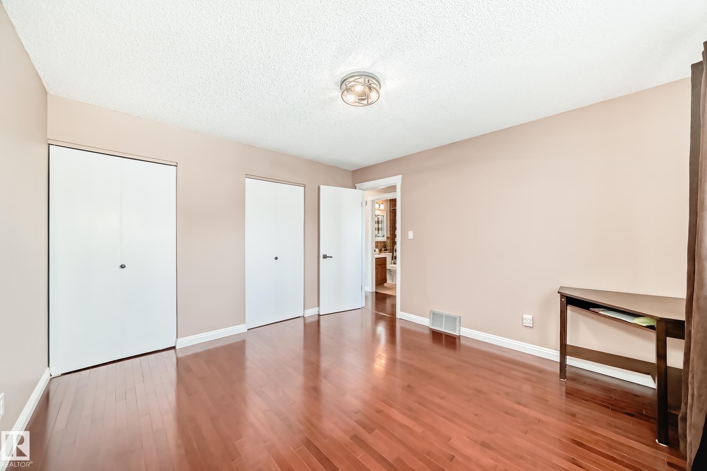 This room features polished hardwood flooring, a ceiling-mounted light fixture, and two white closet doors - 287 Lago Lindo Crescent, Edmonton, AB - Indoor Photo Showing Other Room