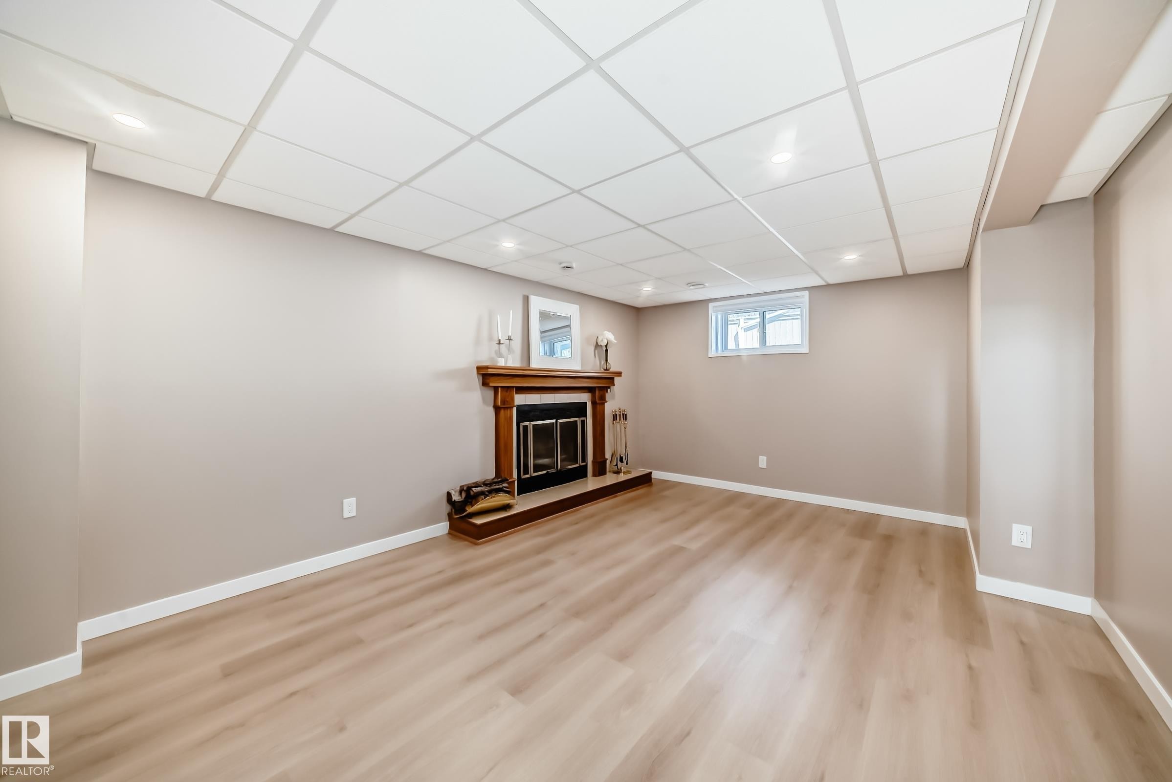 Spacious room featuring light-toned flooring, neutral painted walls, and a fireplace with a wooden mantel - 287 Lago Lindo Crescent, Edmonton, AB - Indoor Photo Showing Basement