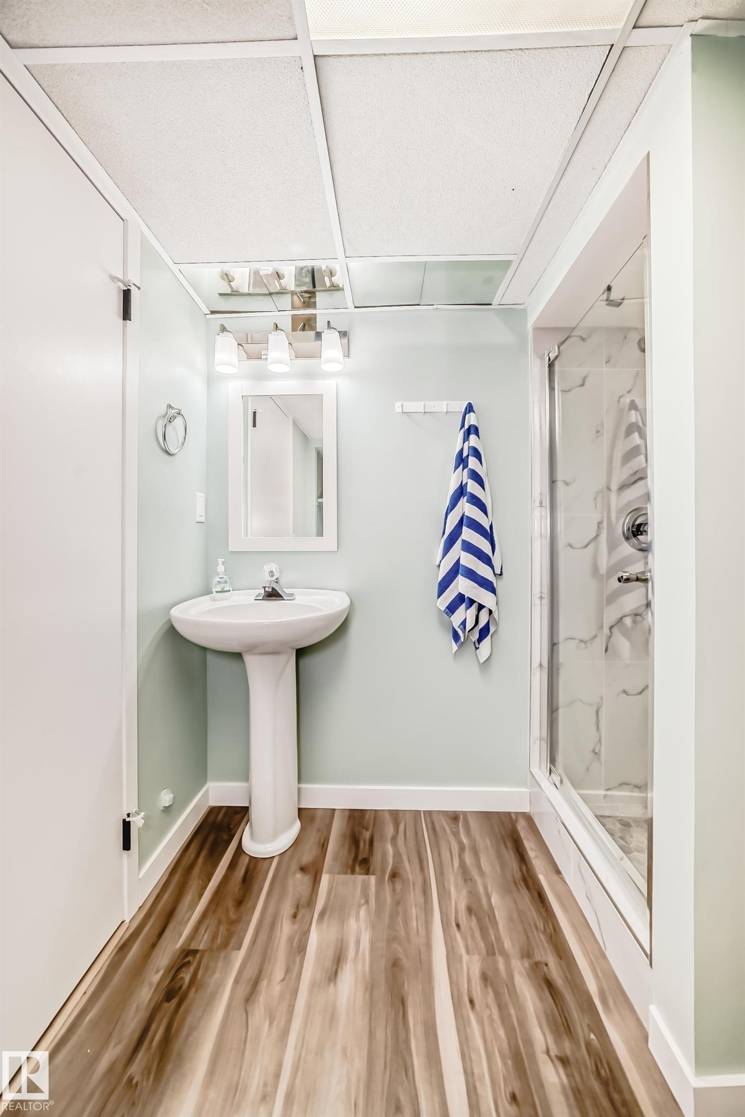 The bathroom features a pedestal sink, a glass-enclosed shower, and wood-look flooring - 287 Lago Lindo Crescent, Edmonton, AB - Indoor Photo Showing Bathroom