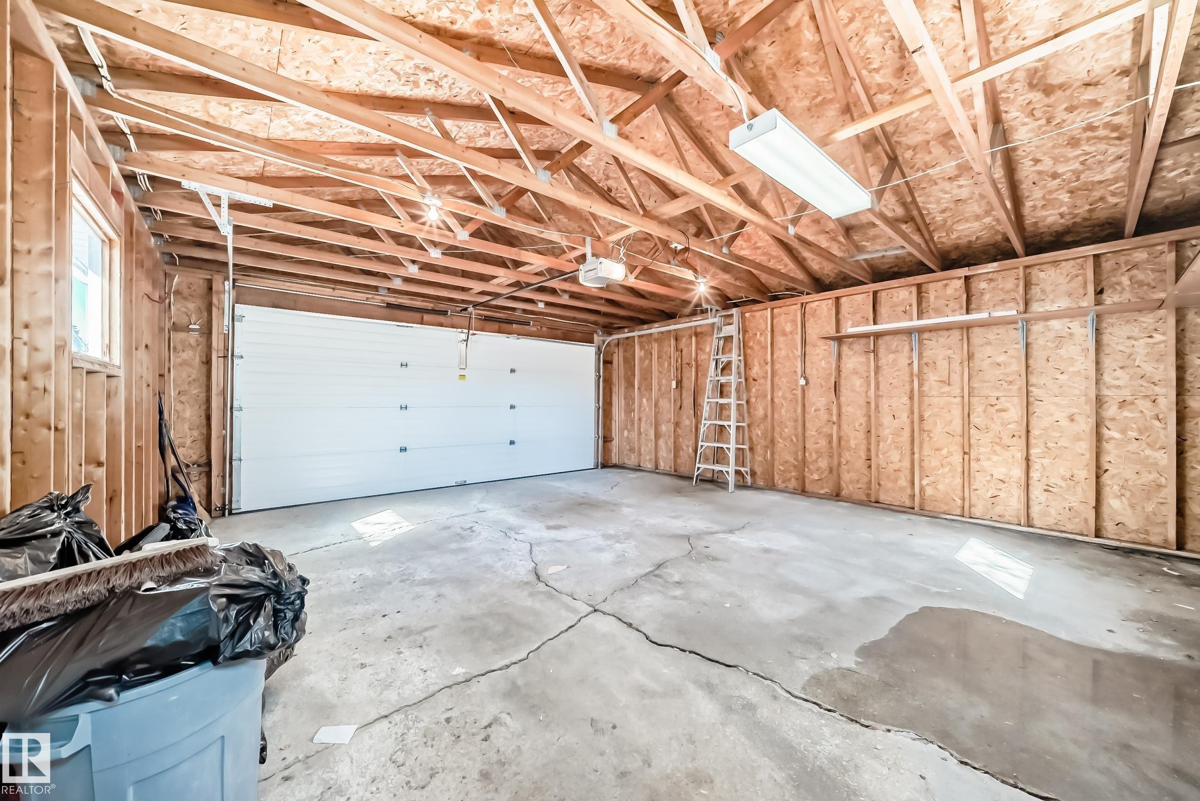 The garage features an overhead sectional door, exposed ceiling joists and rafters, and a concrete floor - 287 Lago Lindo Crescent, Edmonton, AB - Indoor Photo Showing Garage