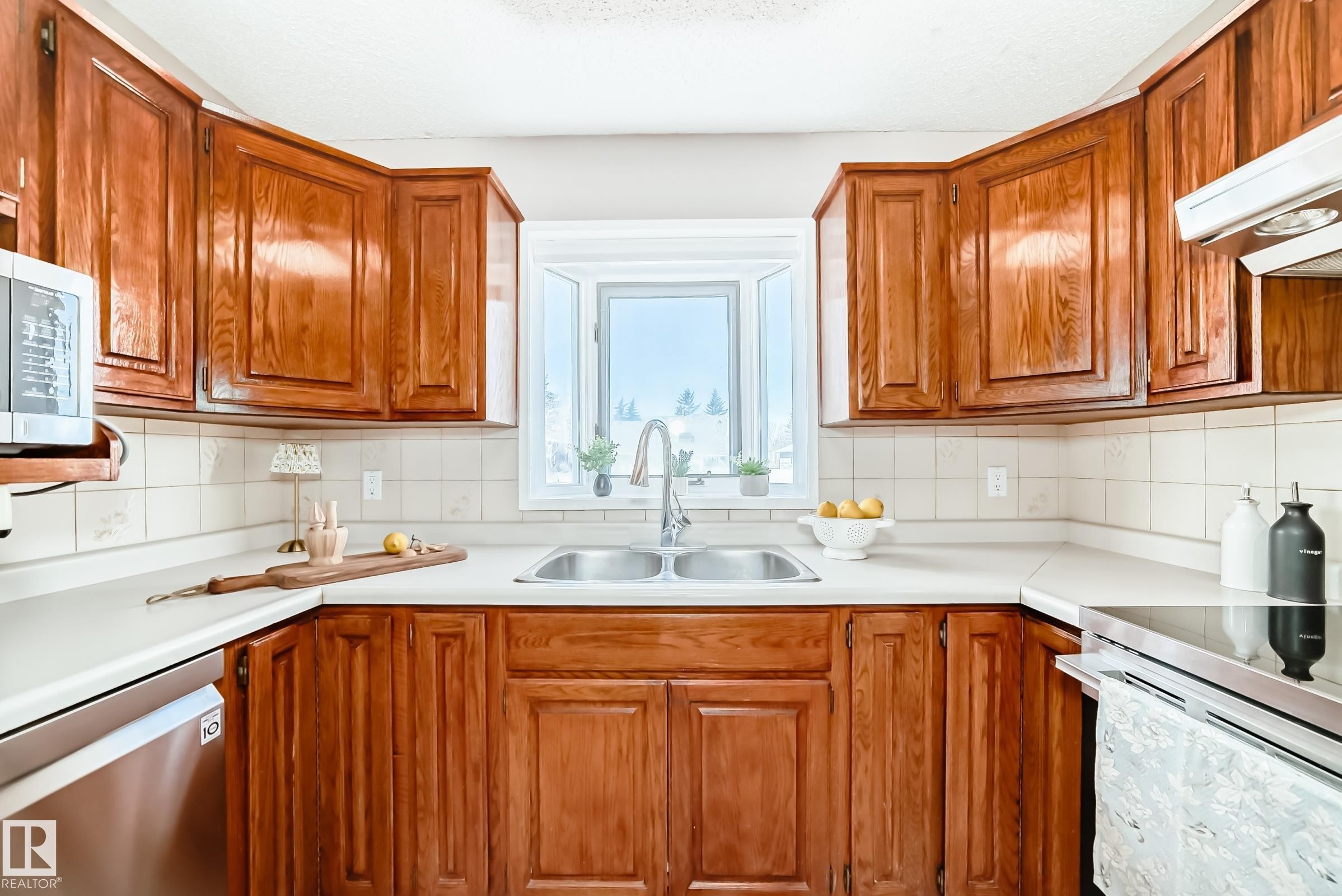 The kitchen features U-shaped wood cabinetry, a double basin stainless steel sink with a single-handle faucet, and a tiled backsplash - 287 Lago Lindo Crescent, Edmonton, AB - Indoor Photo Showing Kitchen With Double Sink