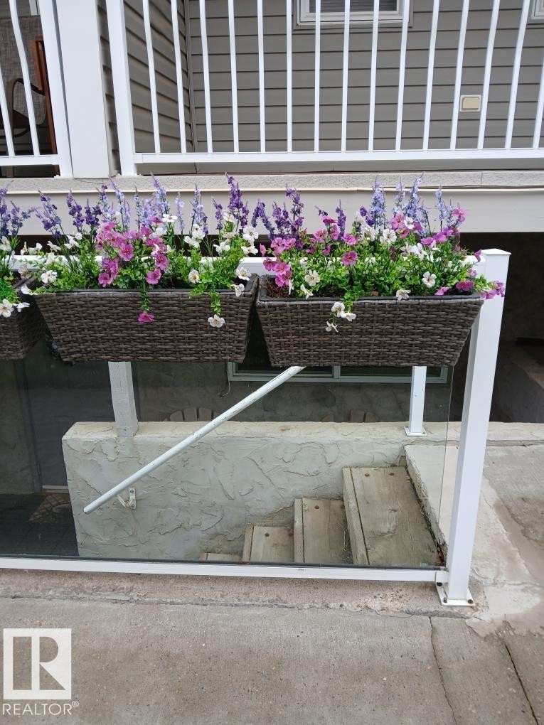 Exterior siding with white baluster railing and planter boxes featuring colorful flowering plants - 5 4902B 43 Street, Legal, AB