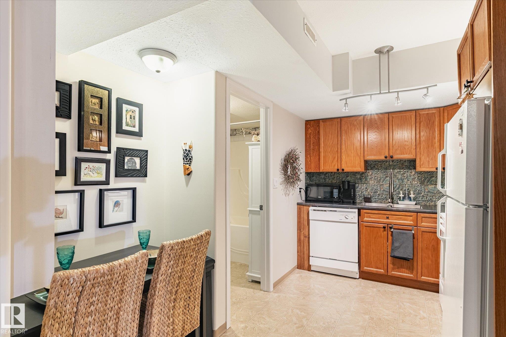 The kitchen features wood cabinetry, a tiled backsplash, and stainless steel sink - 5 4902B 43 Street, Legal, AB
