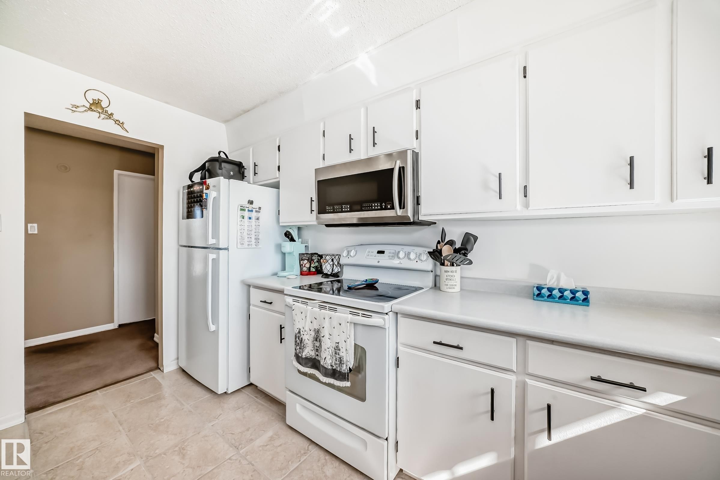 The kitchen features white cabinetry with black hardware, a stainless steel microwave, and a white refrigerator - 11323 162 Avenue, Edmonton, AB - Indoor Photo Showing Kitchen