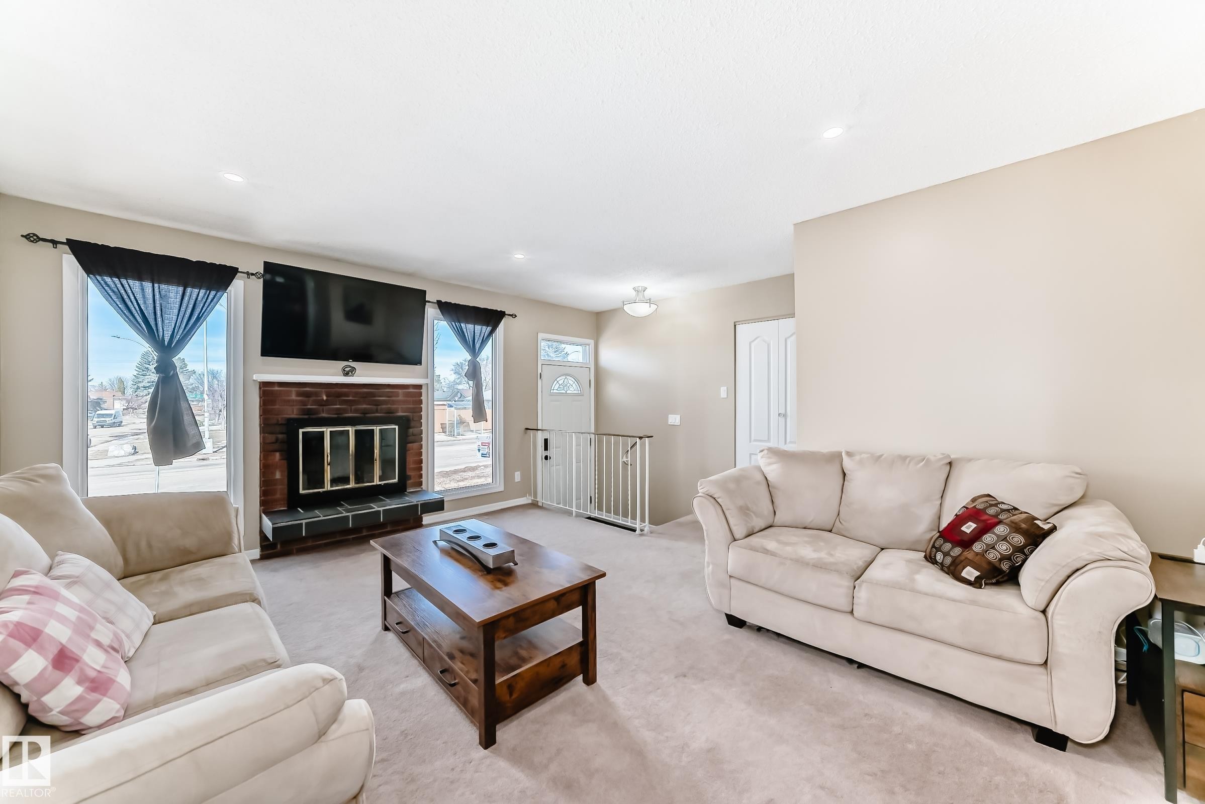 This living area features a brick fireplace, large windows, and neutral-toned walls - 11323 162 Avenue, Edmonton, AB - Indoor Photo Showing Living Room With Fireplace