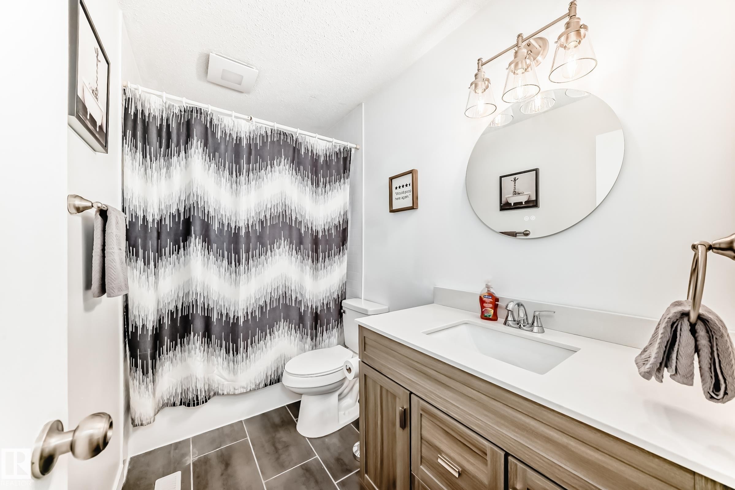 Bathroom featuring a vanity with a white countertop, a circular mirror, and a three-light fixture - 11323 162 Avenue, Edmonton, AB - Indoor Photo Showing Bathroom