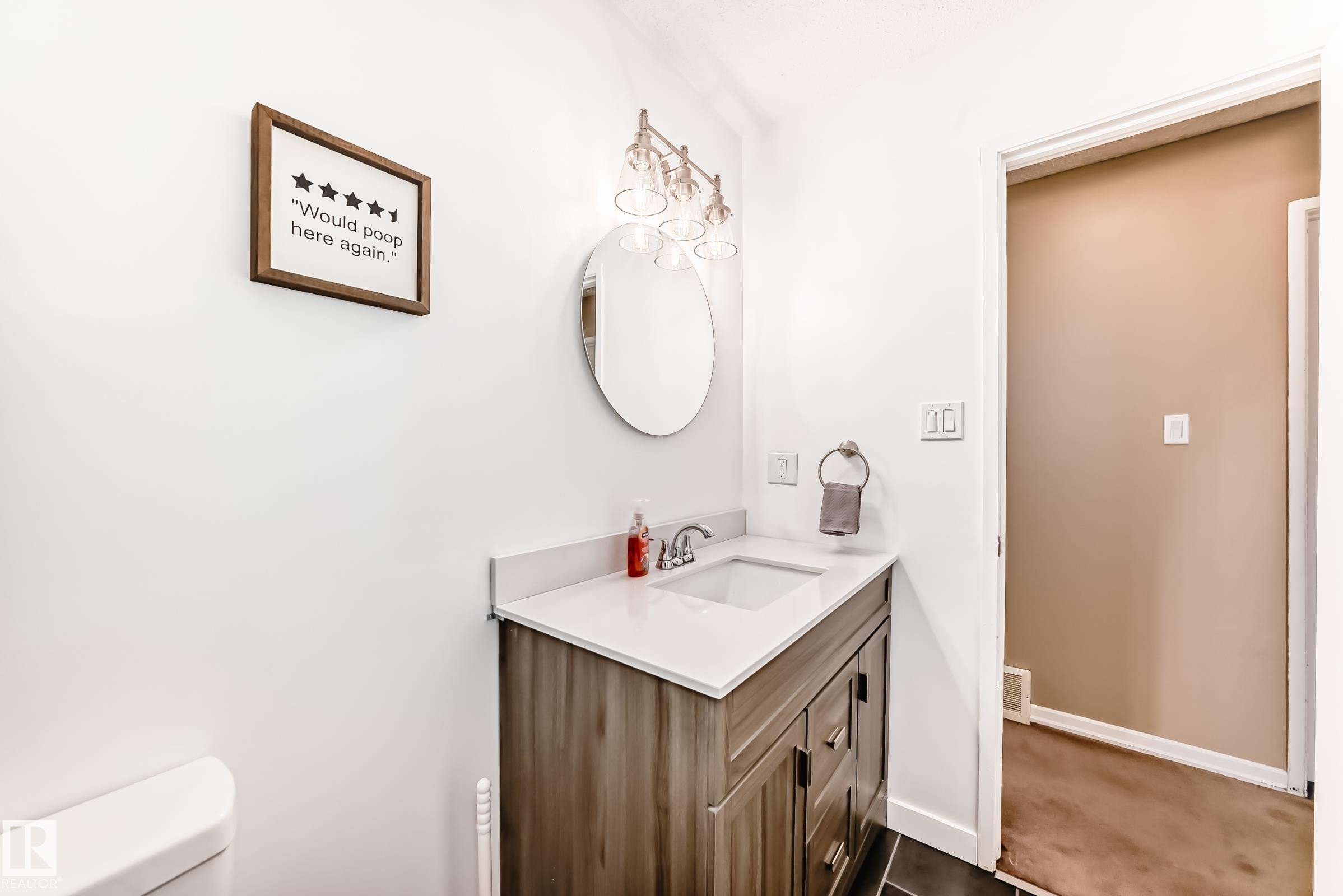 Bathroom featuring a vanity with a white countertop and a dark wood-look cabinet, an oval mirror, and a modern light fixture with clear glass shades - 11323 162 Avenue, Edmonton, AB - Indoor Photo Showing Bathroom