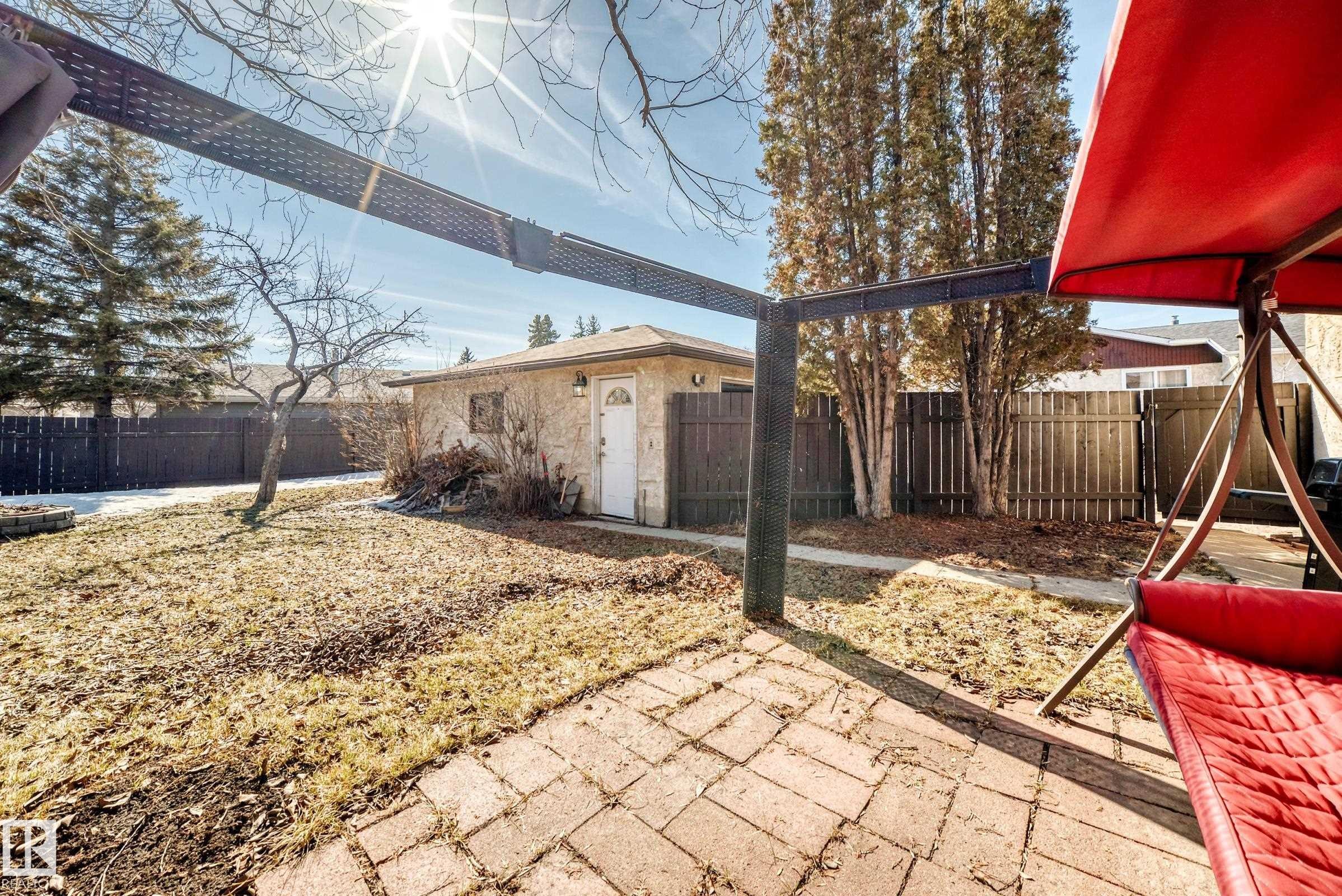 The property features a brick paver patio, a detached garage with a white door, and a fenced yard with mature trees - 11323 162 Avenue, Edmonton, AB - Outdoor