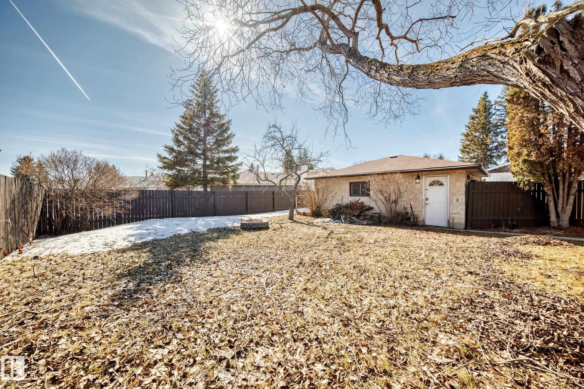 The property features an extensive yard with a wooden fence and a detached structure with a white door and an exterior light fixture - 11323 162 Avenue, Edmonton, AB - Outdoor