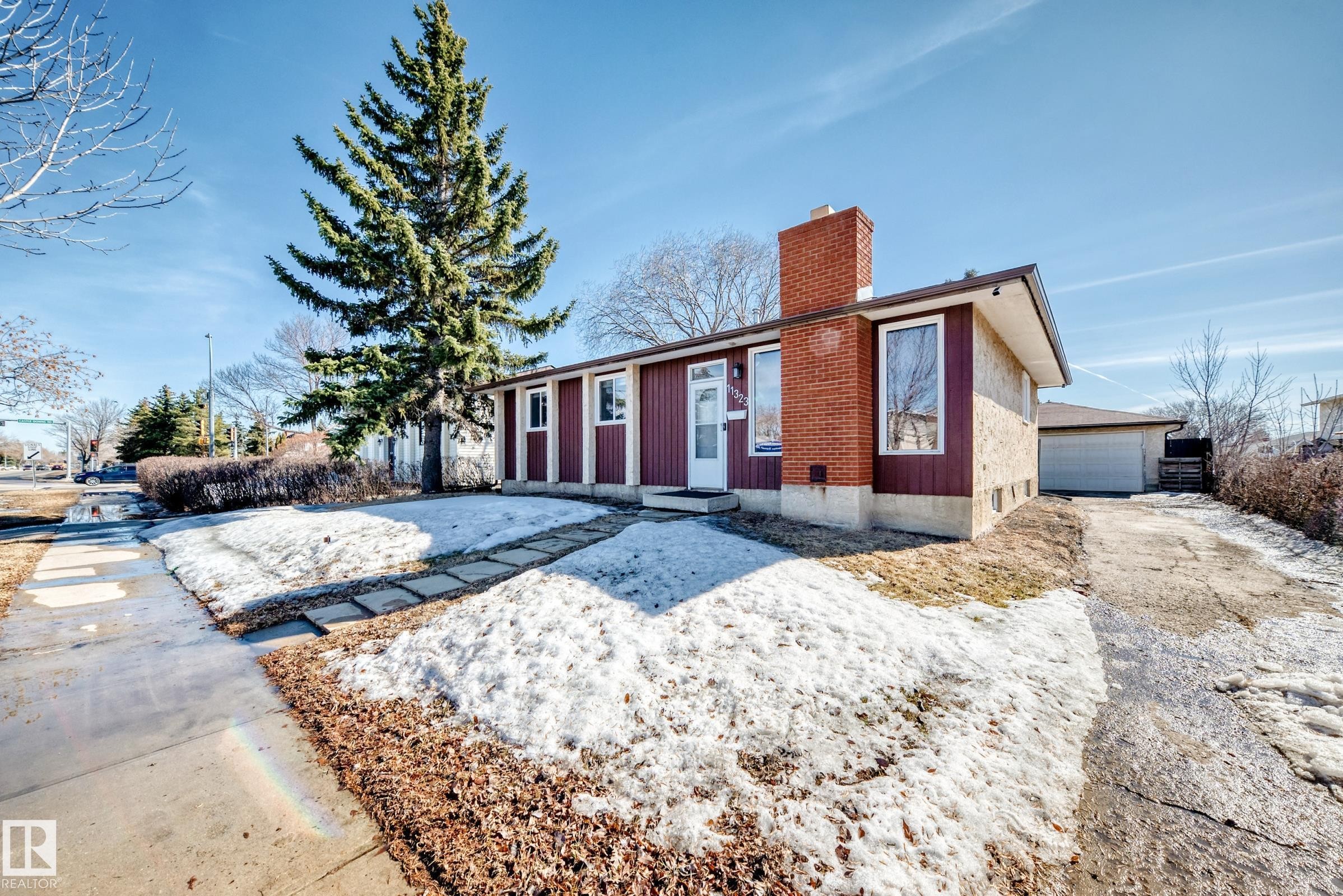 The property features a red brick chimney, a white front door, and a detached garage with a white door, all set on a lot with a paved driveway and a sidewalk - 11323 162 Avenue, Edmonton, AB - Outdoor