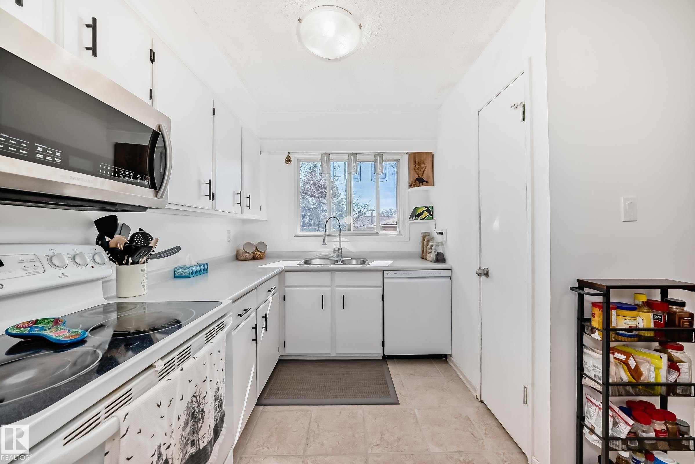 The kitchen features white cabinetry with black hardware, a stainless steel microwave, and an electric range - 11323 162 Avenue, Edmonton, AB - Indoor Photo Showing Kitchen With Double Sink
