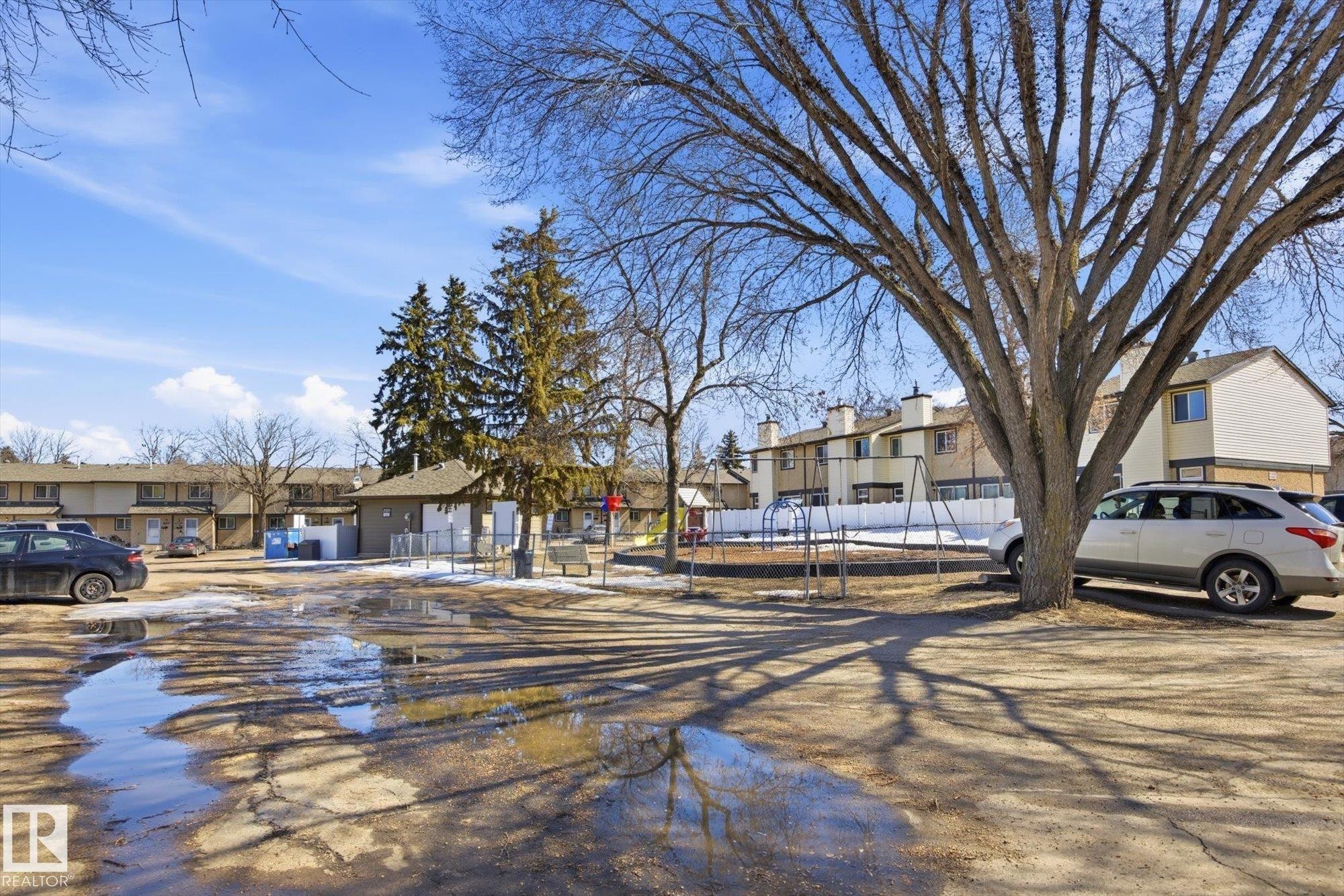 The property features a courtyard area with mature trees and a dedicated playground space, bordered by residential buildings - 3237 142 Avenue, Edmonton, AB - Outdoor