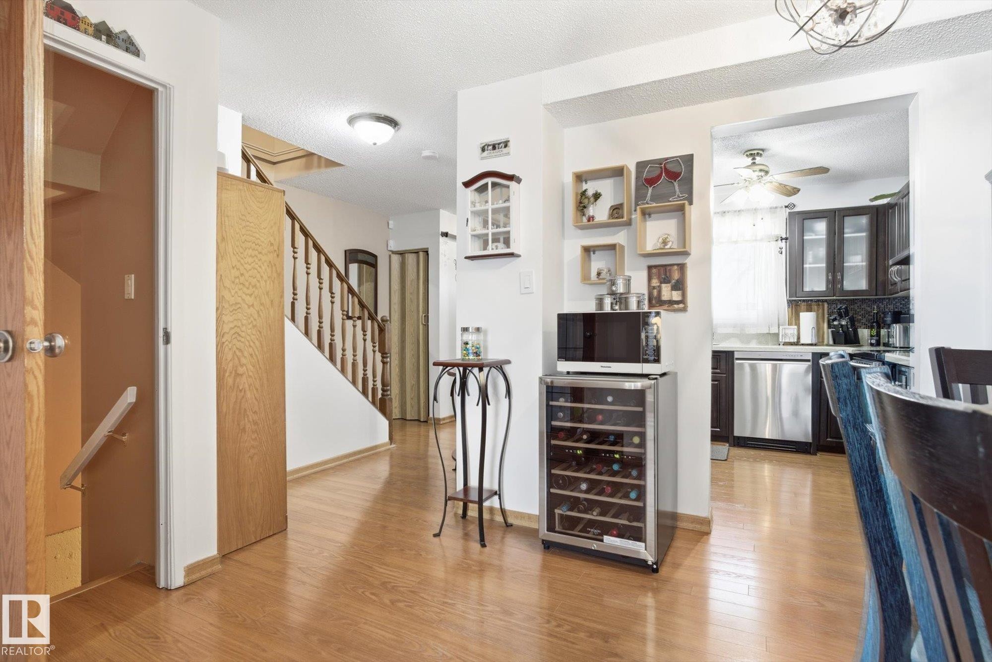 Entryway with hardwood floors and a staircase featuring a wooden handrail, leading to a kitchen with dark cabinetry and stainless steel appliances - 3237 142 Avenue, Edmonton, AB - Indoor