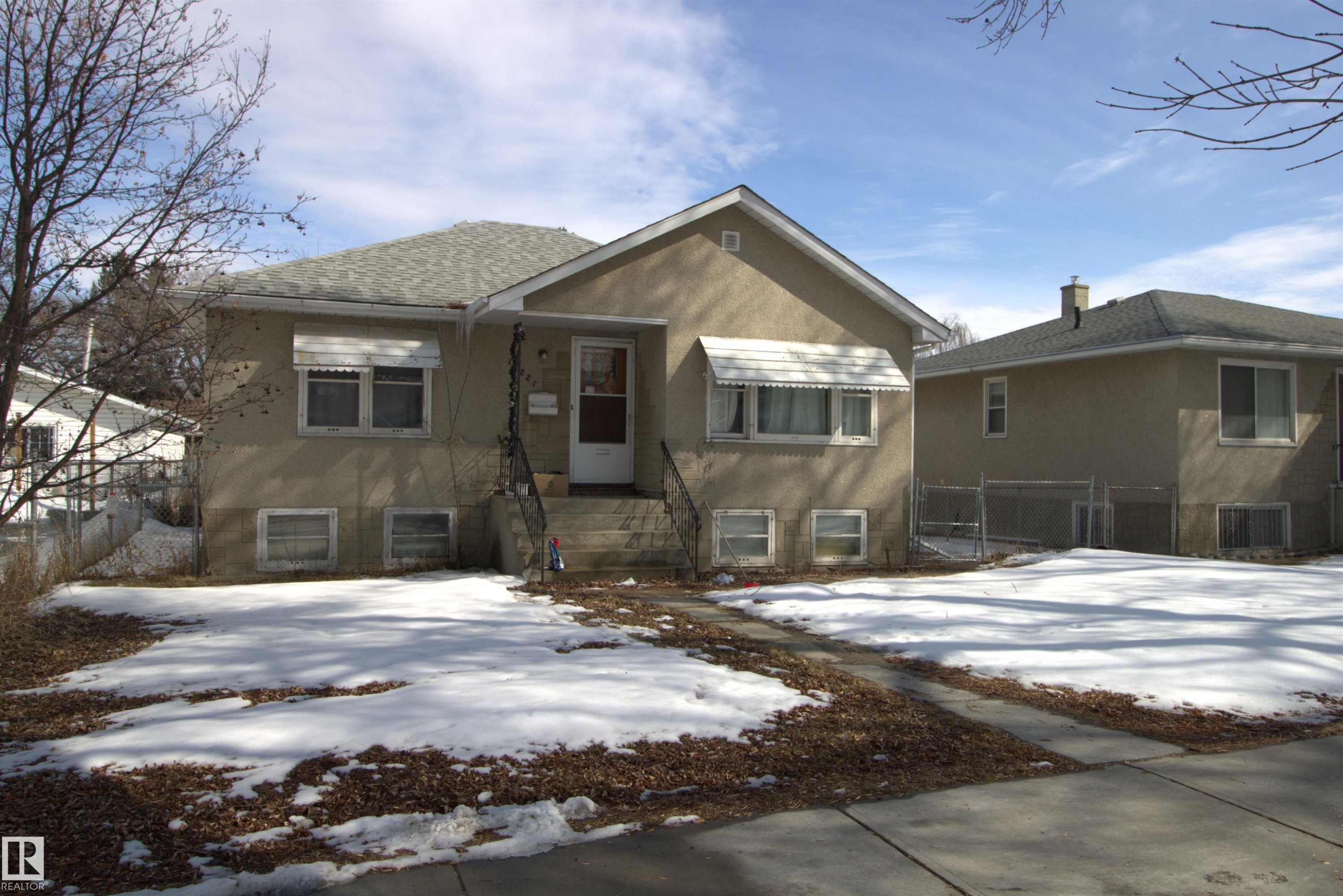 The property features an exterior with light-colored stucco, a gray shingle roof, and a front entryway with dark railings and steps - 12221 94 Street, Edmonton, AB - Outdoor