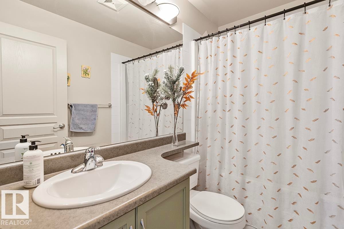 Bathroom featuring a vanity with an integrated sink, a mirror, and a shower with a decorative curtain - 225 16035 132 Street, Edmonton, AB - Indoor Photo Showing Bathroom
