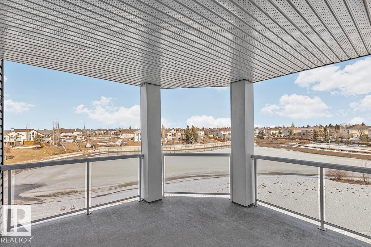 The property features a balcony with a gray floor and a glass railing, offering expansive views of the lake and surrounding homes - 225 16035 132 Street, Edmonton, AB - Outdoor