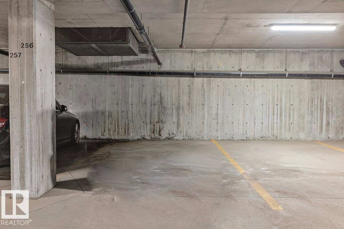 Underground parking space with concrete walls and ceiling, featuring fluorescent lighting and clearly marked parking lines - 225 16035 132 Street, Edmonton, AB - Indoor Photo Showing Garage