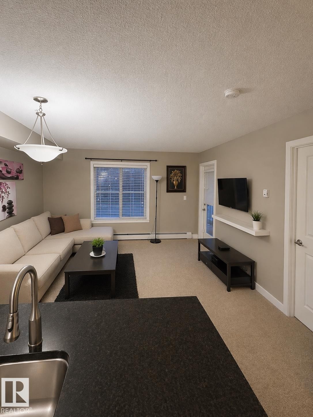 Open concept living area with carpeting, a window with blinds, and a light fixture - 209 107, Watt Commom, Edmonton, AB - Indoor