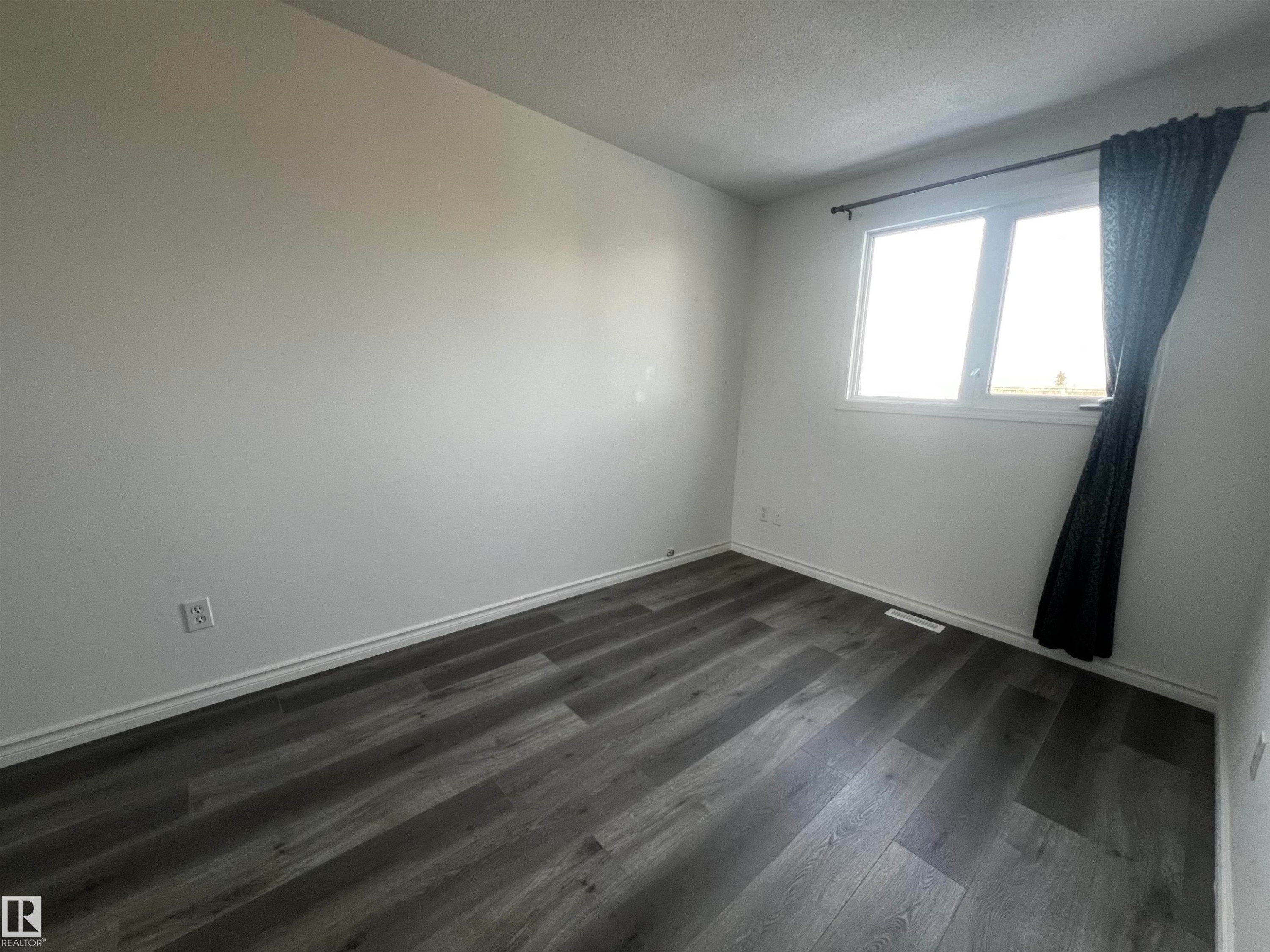 Room featuring light-colored walls, dark-toned flooring, and a window with a dark curtain - 3323 107 Avenue Nw, Edmonton, AB - Indoor Photo Showing Other Room