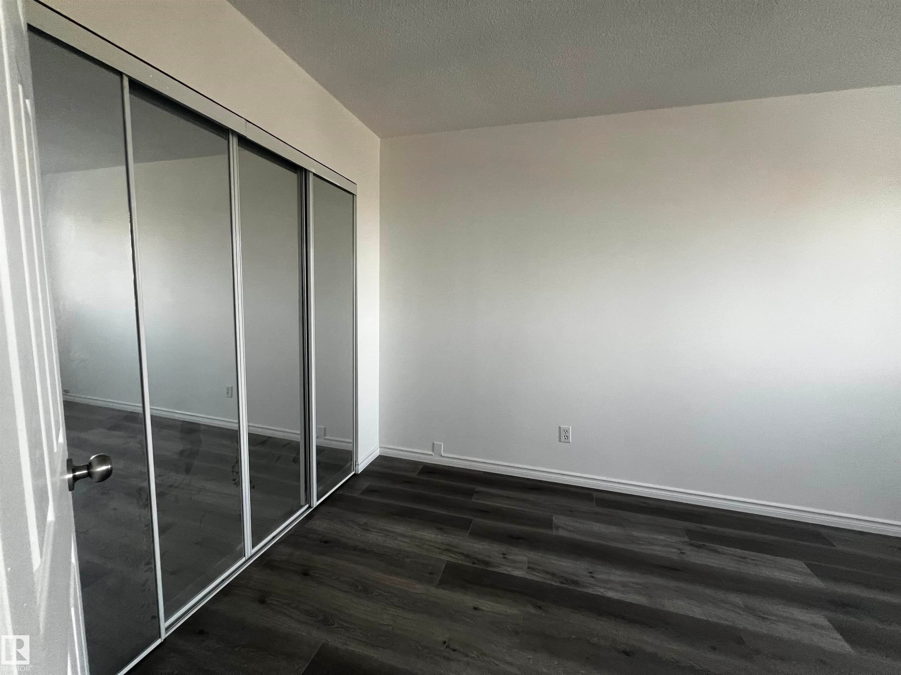 This room features dark wood-look flooring and a closet with mirrored sliding doors - 3323 107 Avenue Nw, Edmonton, AB - Indoor Photo Showing Other Room