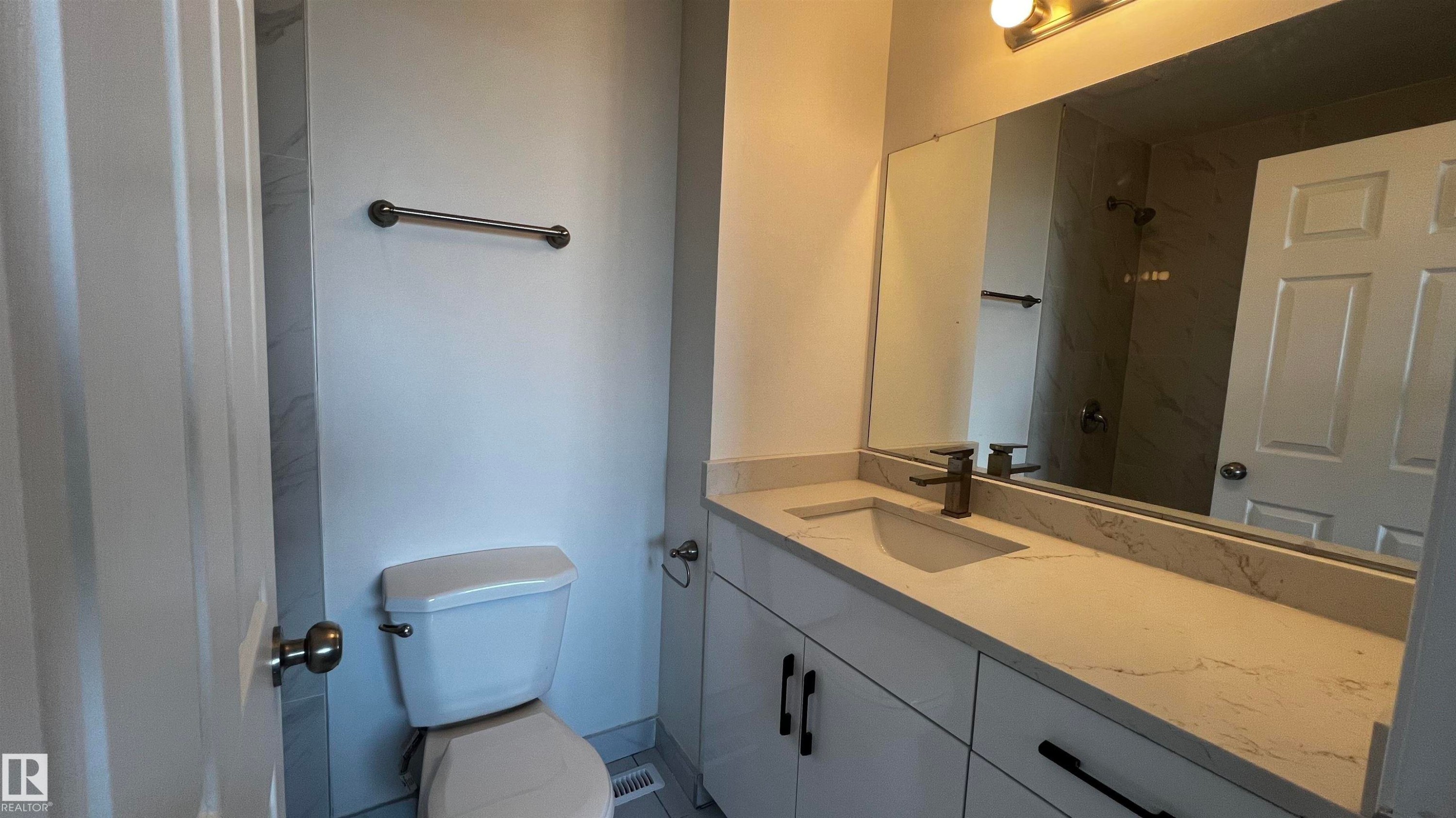 Bathroom featuring a vanity with a light-colored countertop and integrated sink, a large mirror, and a toilet - 3323 107 Avenue Nw, Edmonton, AB - Indoor Photo Showing Bathroom