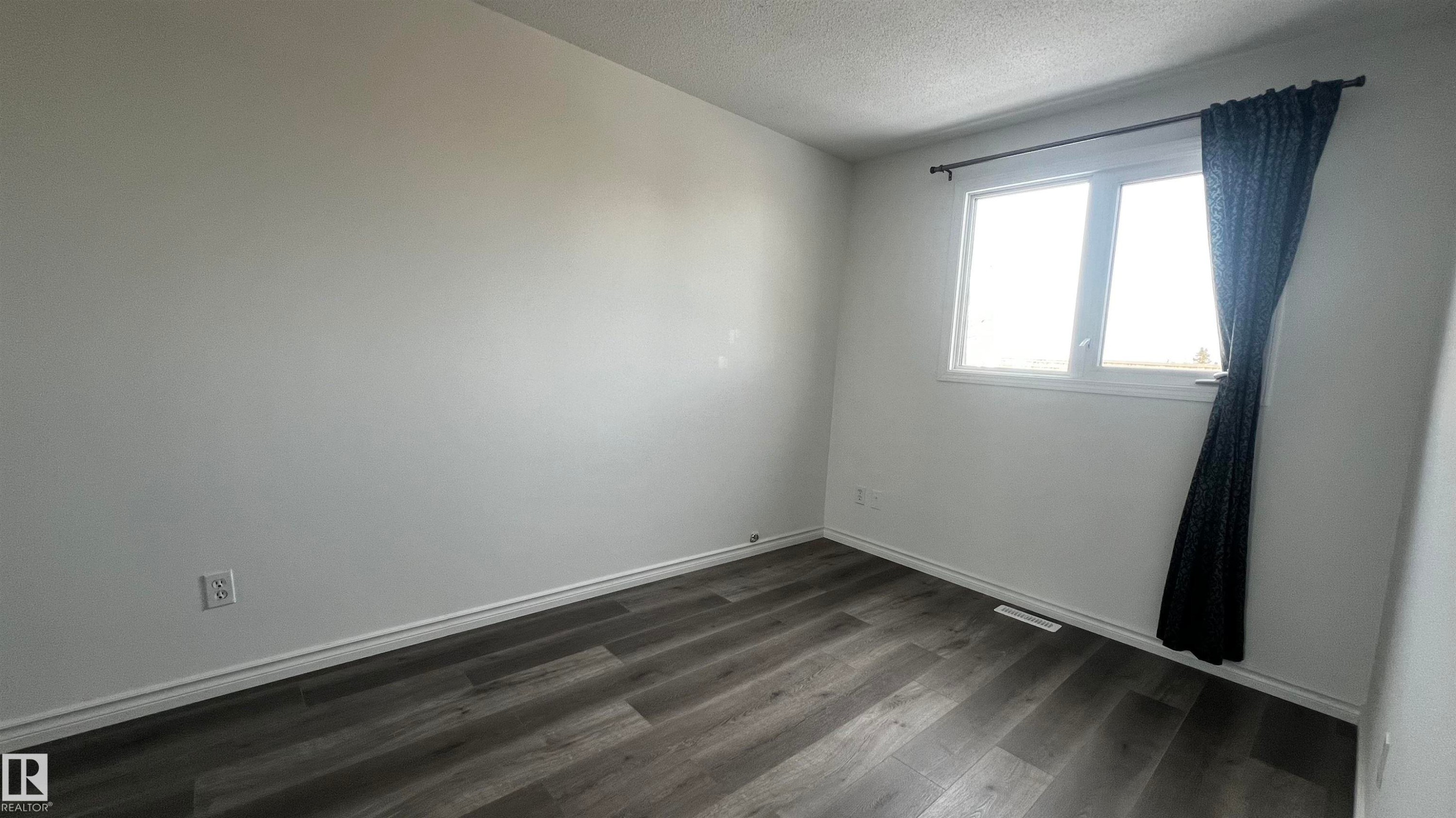 This room features light-colored walls, dark wood-style flooring, and a window with a curtain rod - 3323 107 Avenue Nw, Edmonton, AB - Indoor Photo Showing Other Room