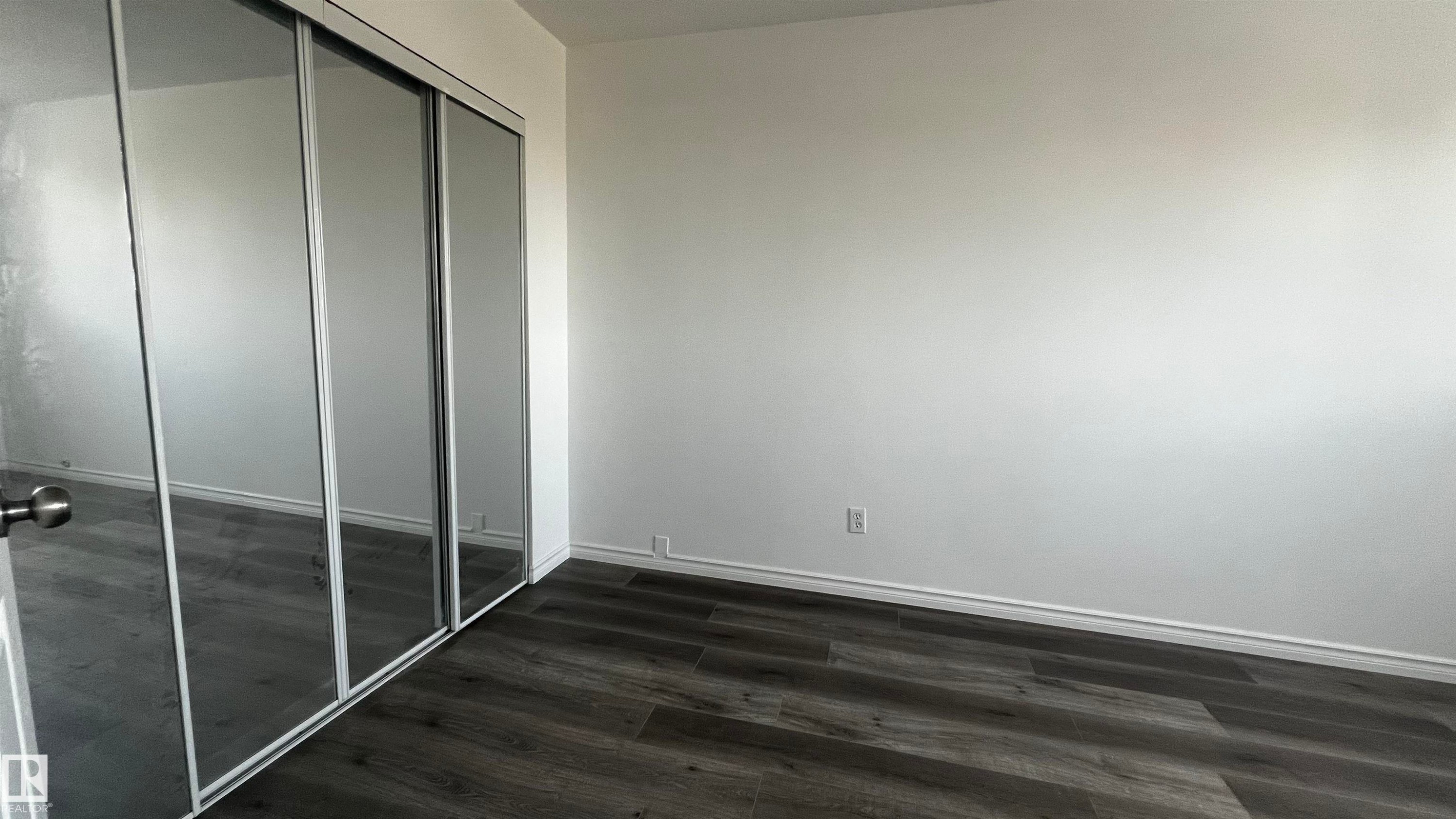 Room featuring wood-look flooring and a mirrored closet with sliding doors - 3323 107 Avenue Nw, Edmonton, AB - Indoor Photo Showing Other Room