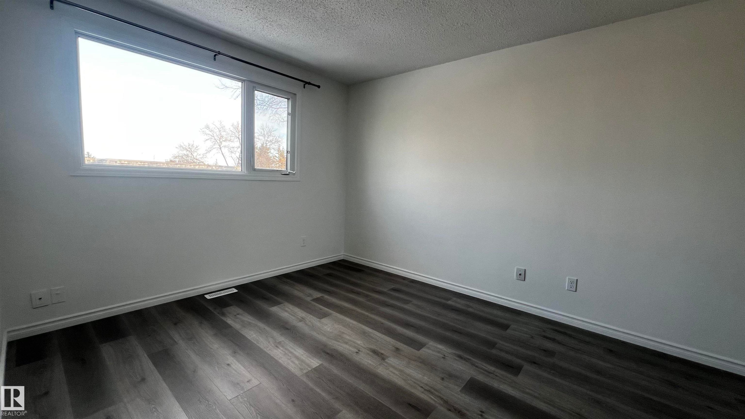 Room featuring wood-look flooring, white walls, and a window providing natural light - 3323 107 Avenue Nw, Edmonton, AB - Indoor Photo Showing Other Room
