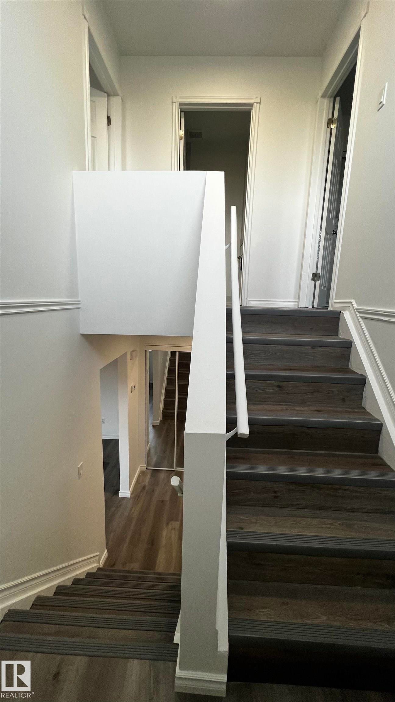 Staircase featuring wood-look flooring with dark treads and white risers, complemented by a white handrail and baseboards - 3323 107 Avenue Nw, Edmonton, AB - Indoor Photo Showing Other Room