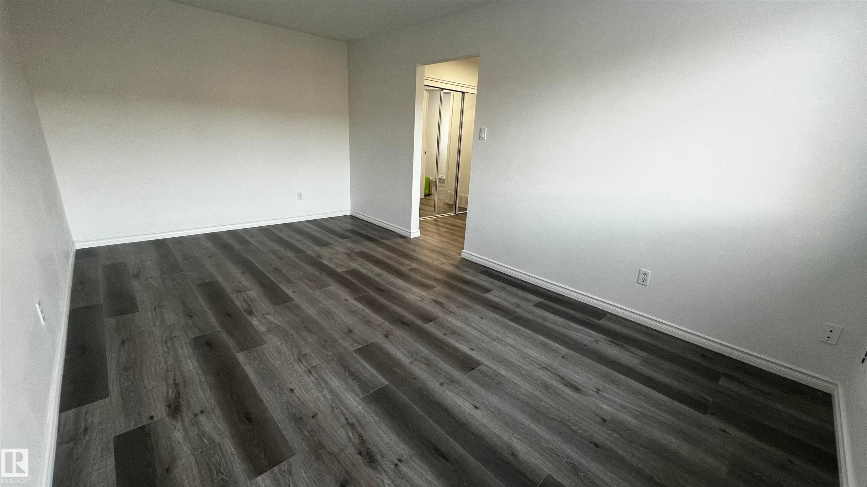 This room features dark wood-style flooring and white walls, offering a bright and versatile space - 3323 107 Avenue Nw, Edmonton, AB - Indoor Photo Showing Other Room