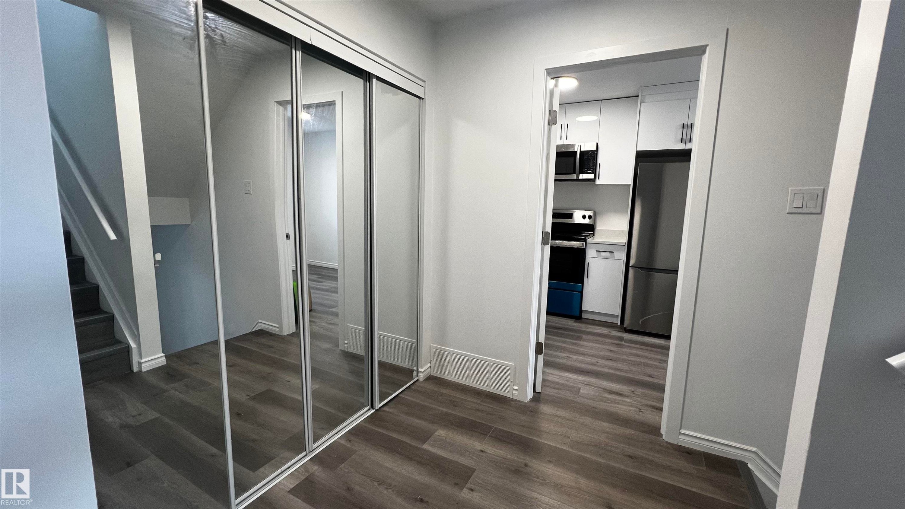 This property features gray wood-look flooring, a kitchen with white cabinetry and stainless steel appliances, and a closet with mirrored sliding doors - 3323 107 Avenue Nw, Edmonton, AB - Indoor Photo Showing Other Room