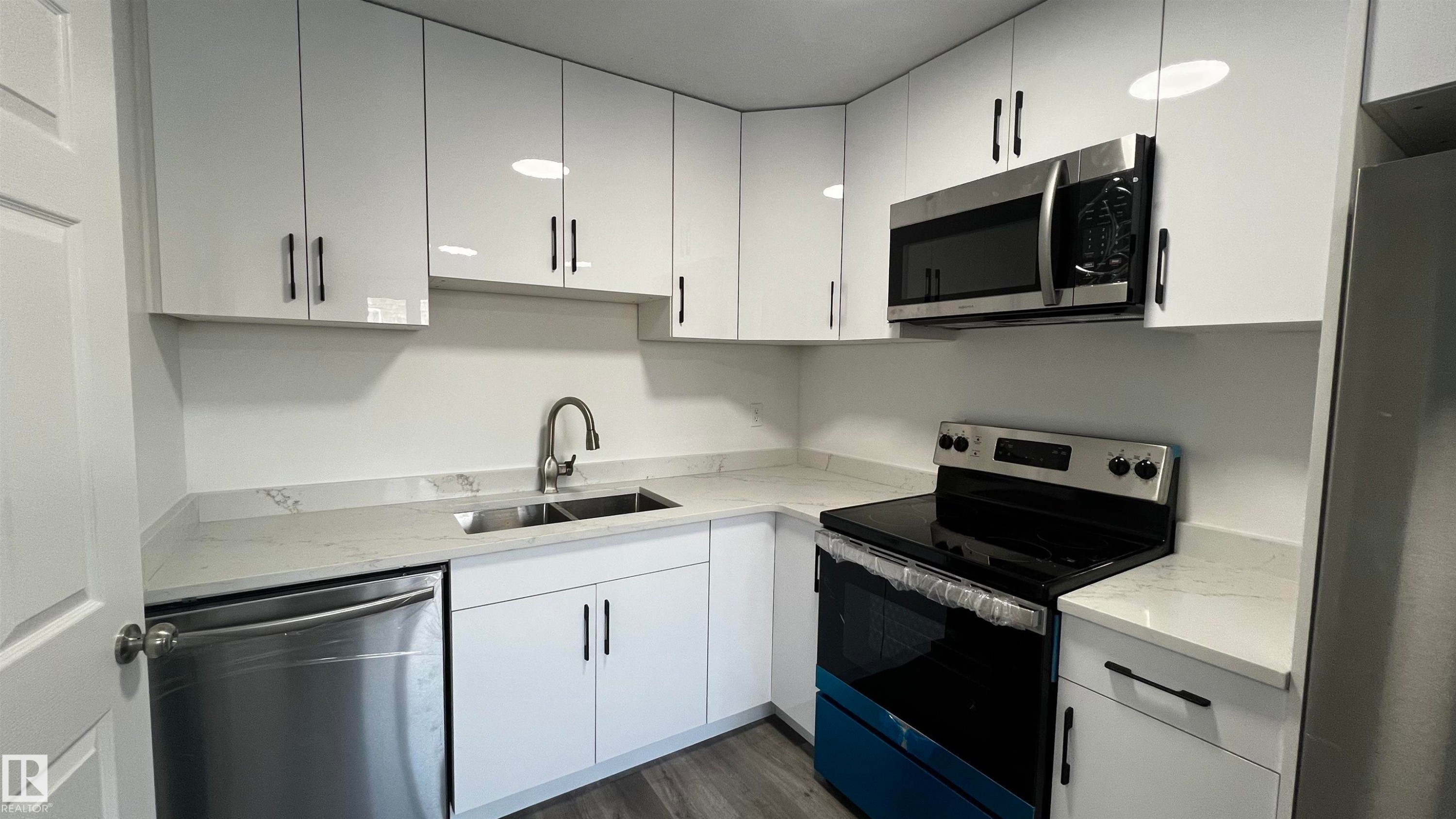 The kitchen features white cabinetry, white countertops, and stainless steel appliances including a microwave, dishwasher, and stove - 3323 107 Avenue Nw, Edmonton, AB - Indoor Photo Showing Kitchen With Double Sink