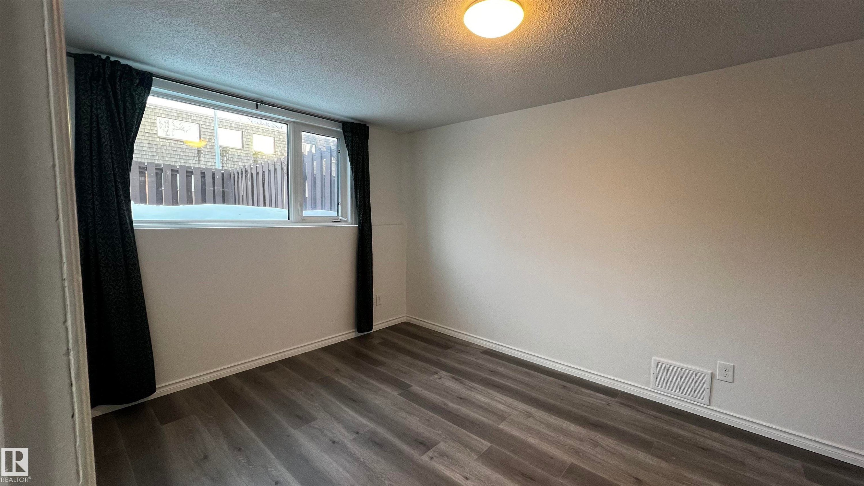 This room features durable plank flooring, a neutral wall color, and a window with dark curtains - 3323 107 Avenue Nw, Edmonton, AB - Indoor Photo Showing Other Room