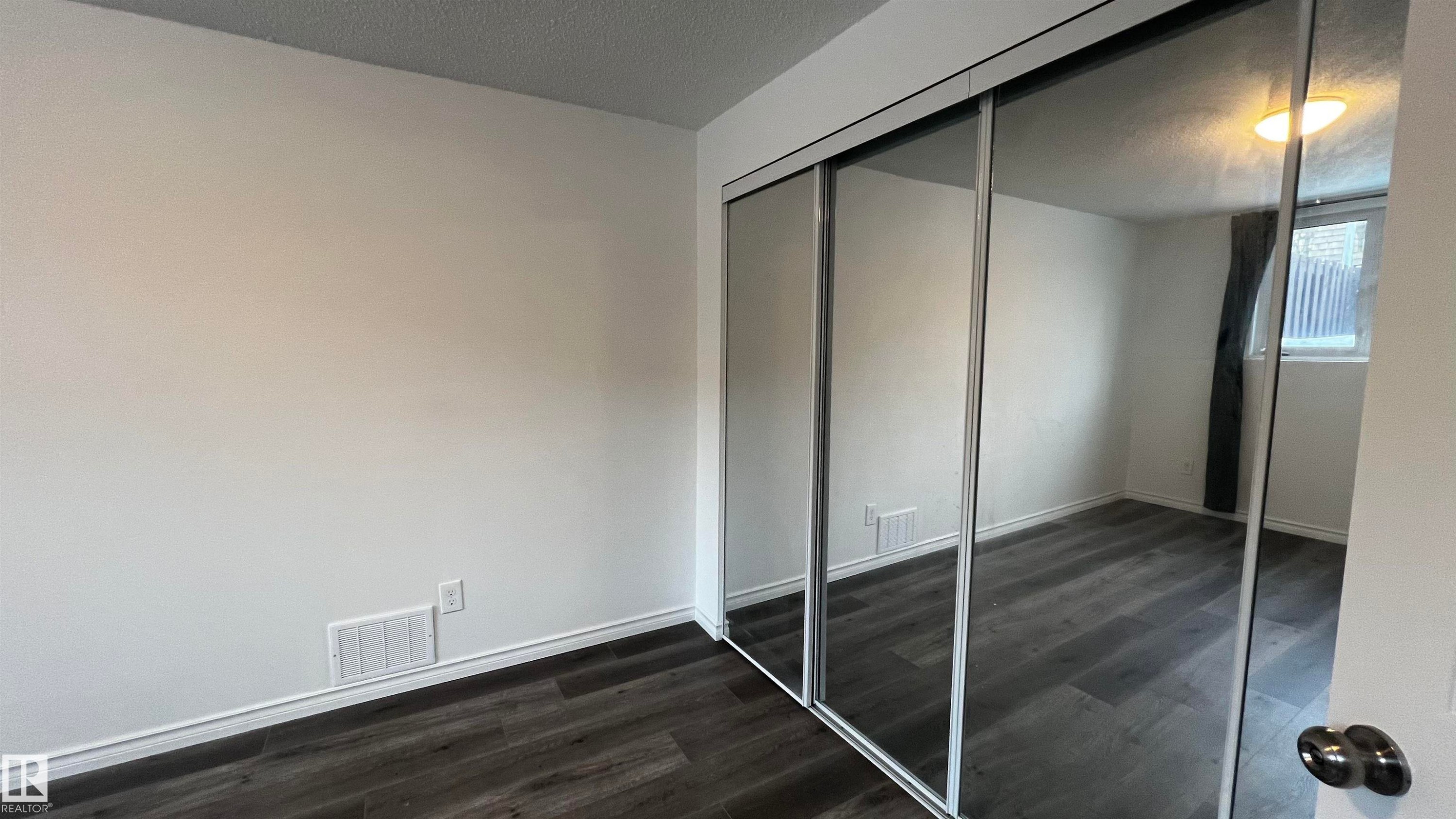 This room features dark-toned flooring, white walls, and mirrored closet doors - 3323 107 Avenue Nw, Edmonton, AB - Indoor Photo Showing Other Room
