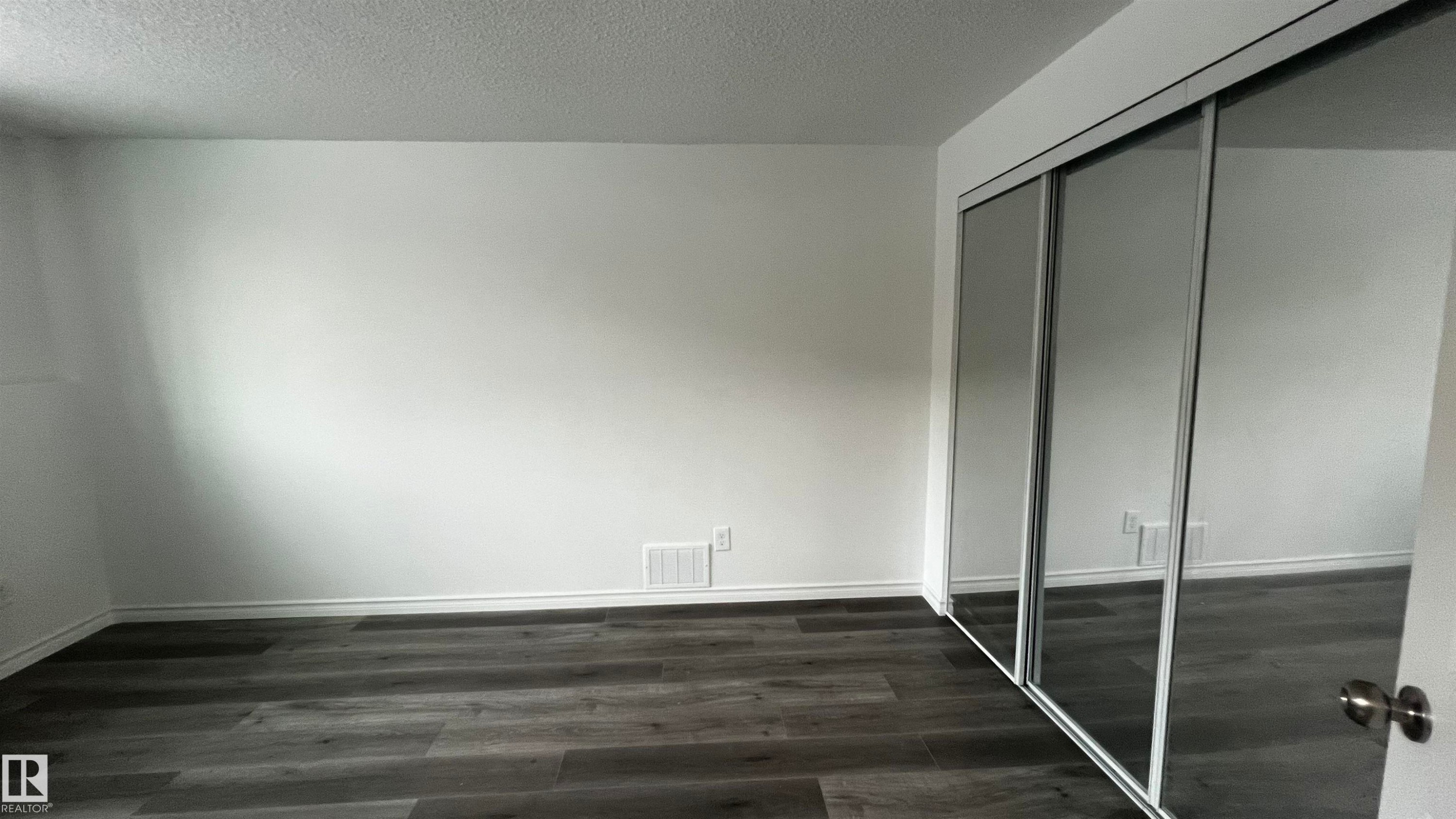 Bedroom featuring dark wood-style flooring and mirrored closet doors - 3323 107 Avenue Nw, Edmonton, AB - Indoor Photo Showing Other Room