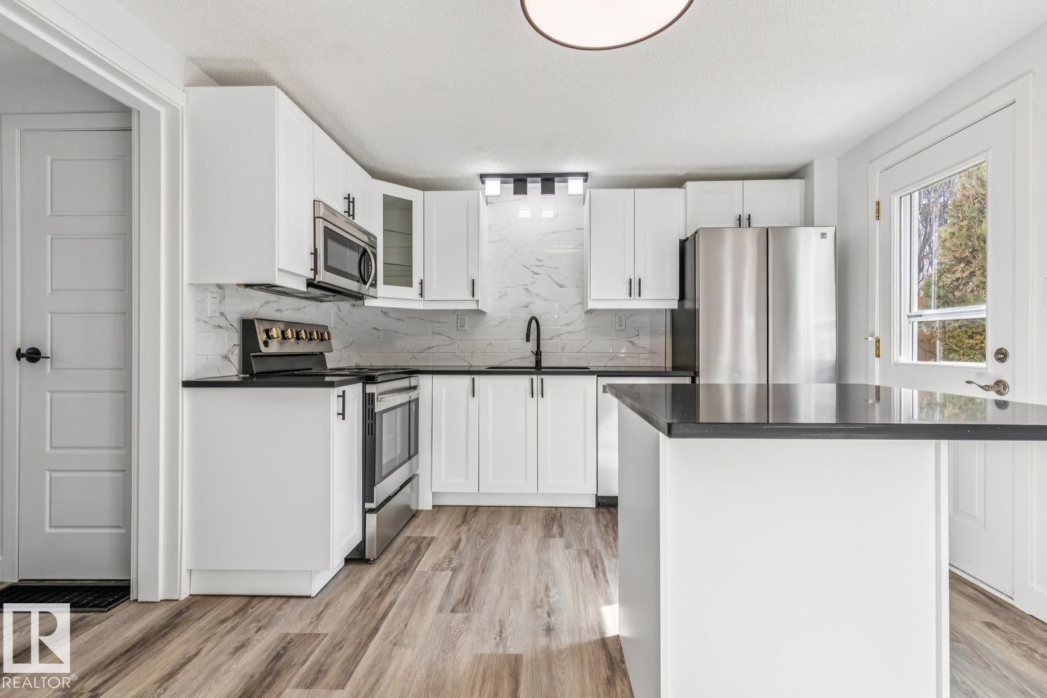 The kitchen features white cabinetry, stainless steel appliances, dark countertops, a tiled backsplash, and wood-look flooring - 95 Ridgewood Terrace, St. Albert, AB - Indoor Photo Showing Kitchen With Stainless Steel Kitchen With Upgraded Kitchen