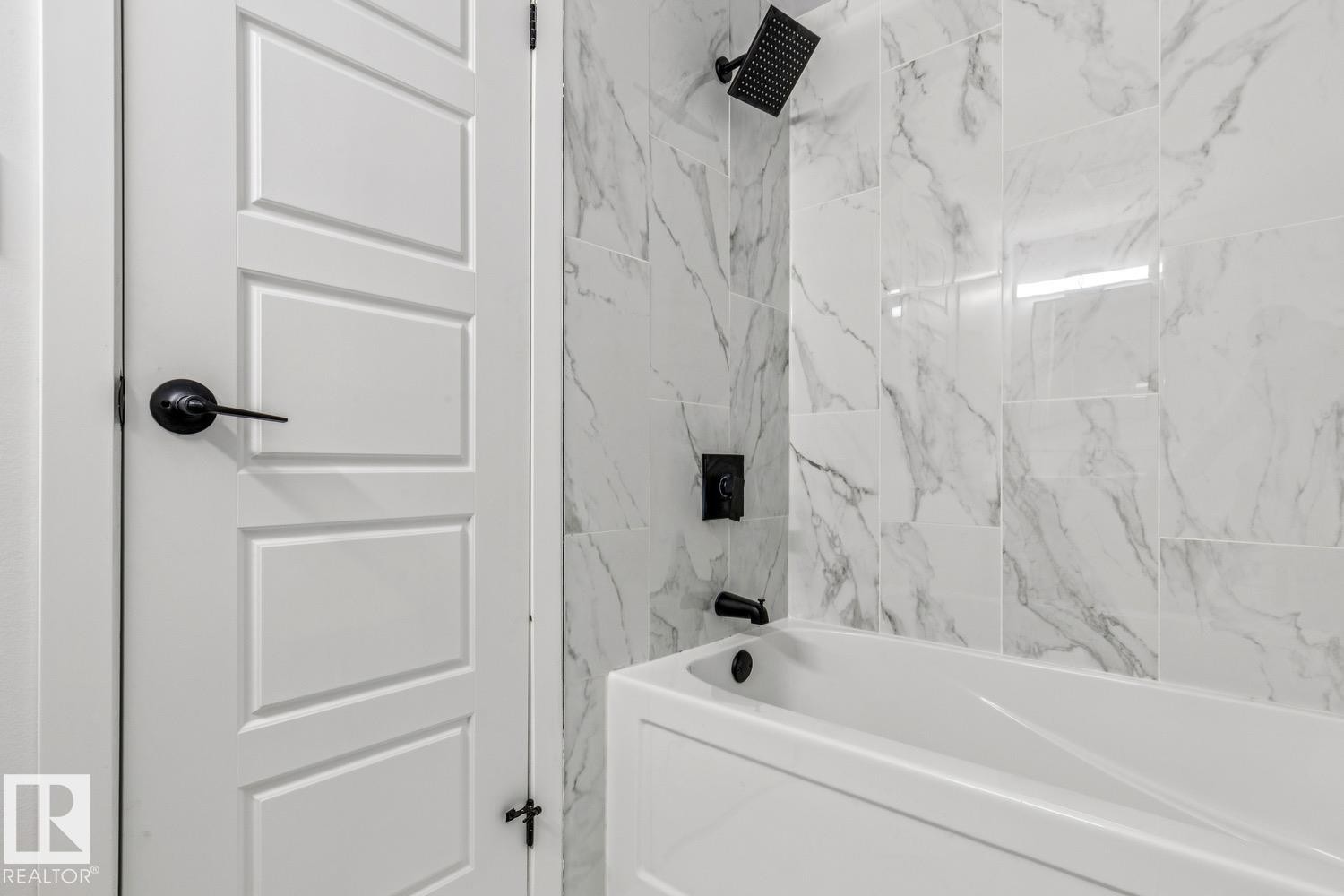 The bathroom features a white bathtub with white and gray marble-patterned tile surround, complete with a matte black showerhead and faucet - 95 Ridgewood Terrace, St. Albert, AB - Indoor Photo Showing Bathroom