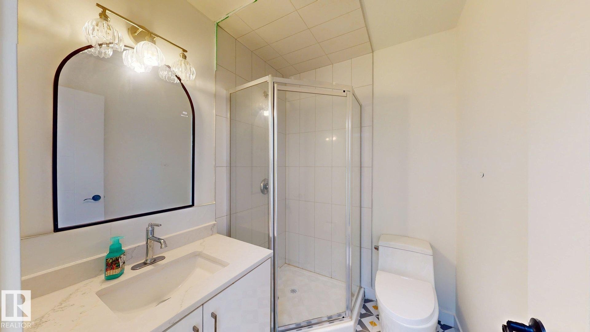 Bathroom featuring a vanity with an integrated sink, a framed mirror, and a glass-enclosed shower with tiled walls - 8515 86 Avenue, Edmonton, AB - Indoor Photo Showing Bathroom