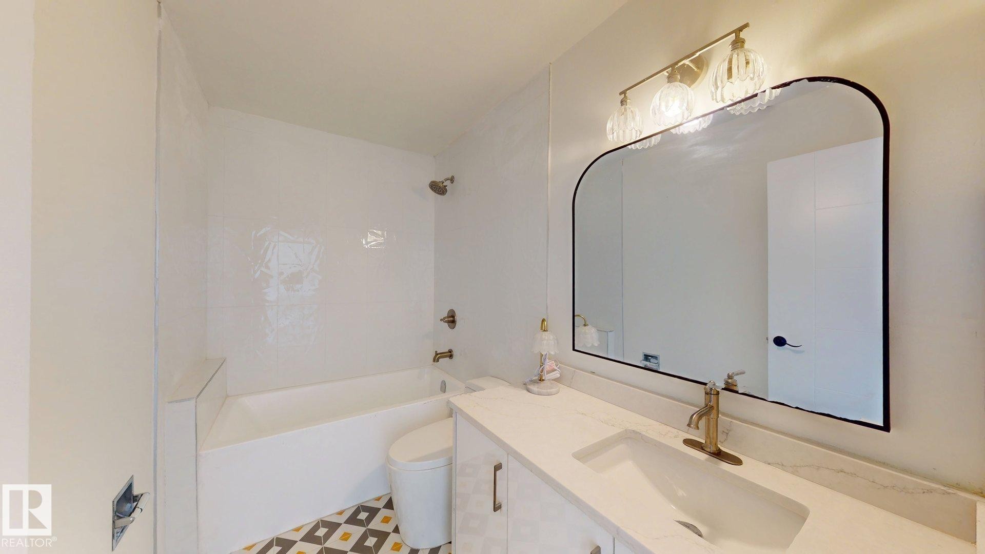 Bathroom featuring a white vanity with a rectangular undermount sink, a large arched mirror, and a combination bathtub and shower with white subway tile surround - 8515 86 Avenue, Edmonton, AB - Indoor Photo Showing Bathroom