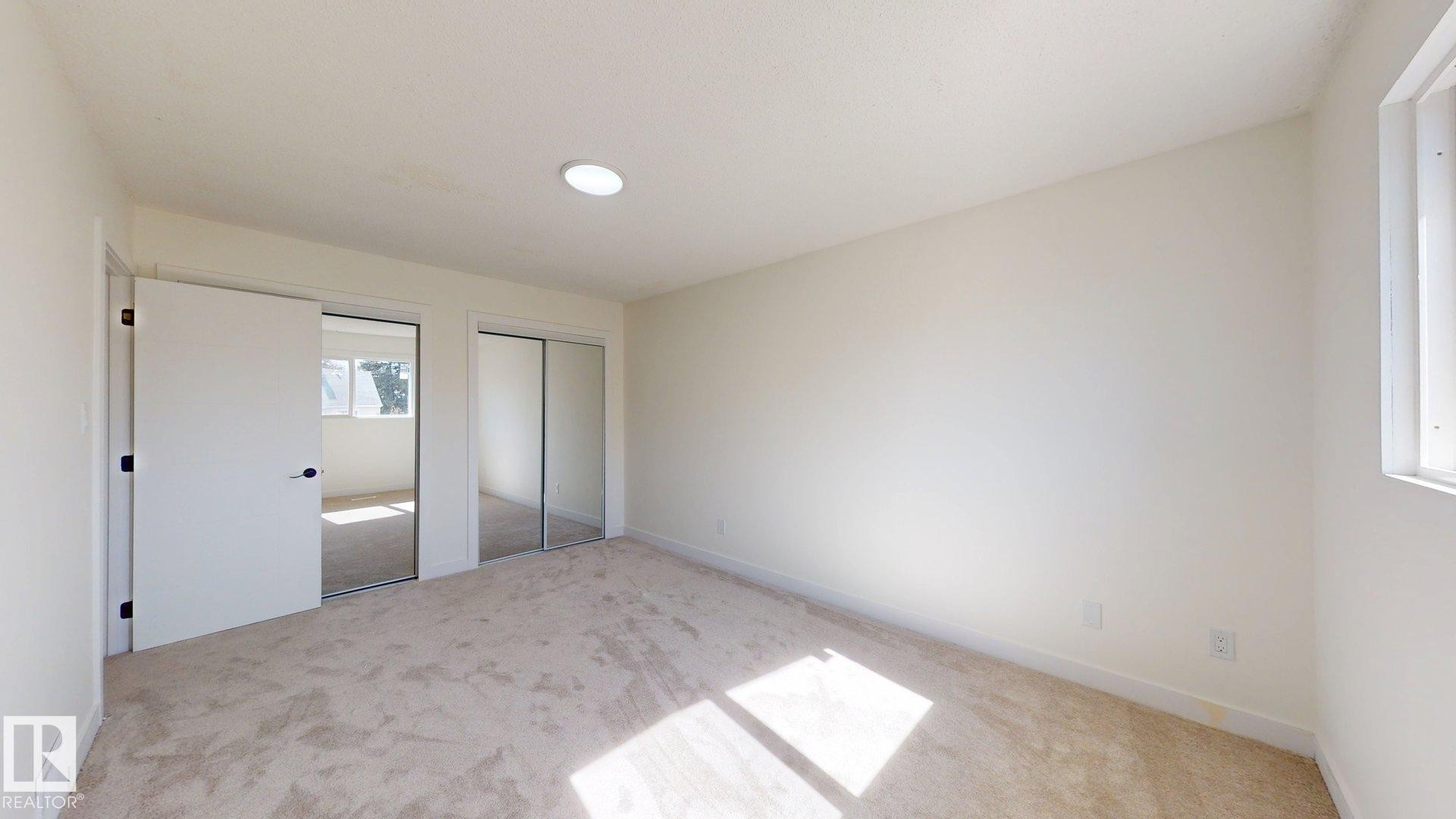 This room features light-colored carpeting, a window, and a closet with mirrored sliding doors - 8515 86 Avenue, Edmonton, AB - Indoor Photo Showing Other Room