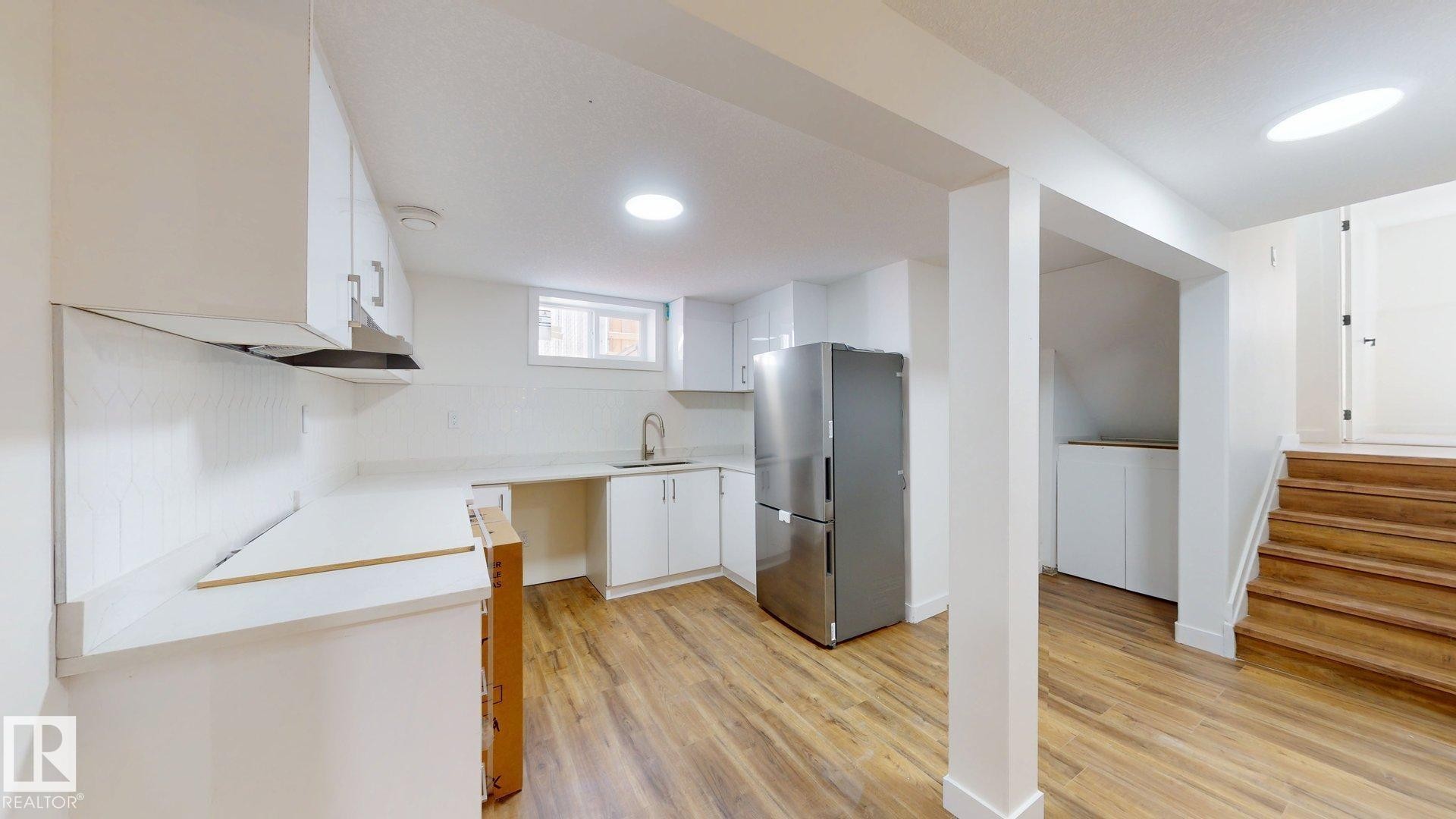 Kitchen area featuring white cabinetry, a stainless steel refrigerator, and wood-look flooring - 8515 86 Avenue, Edmonton, AB - Indoor