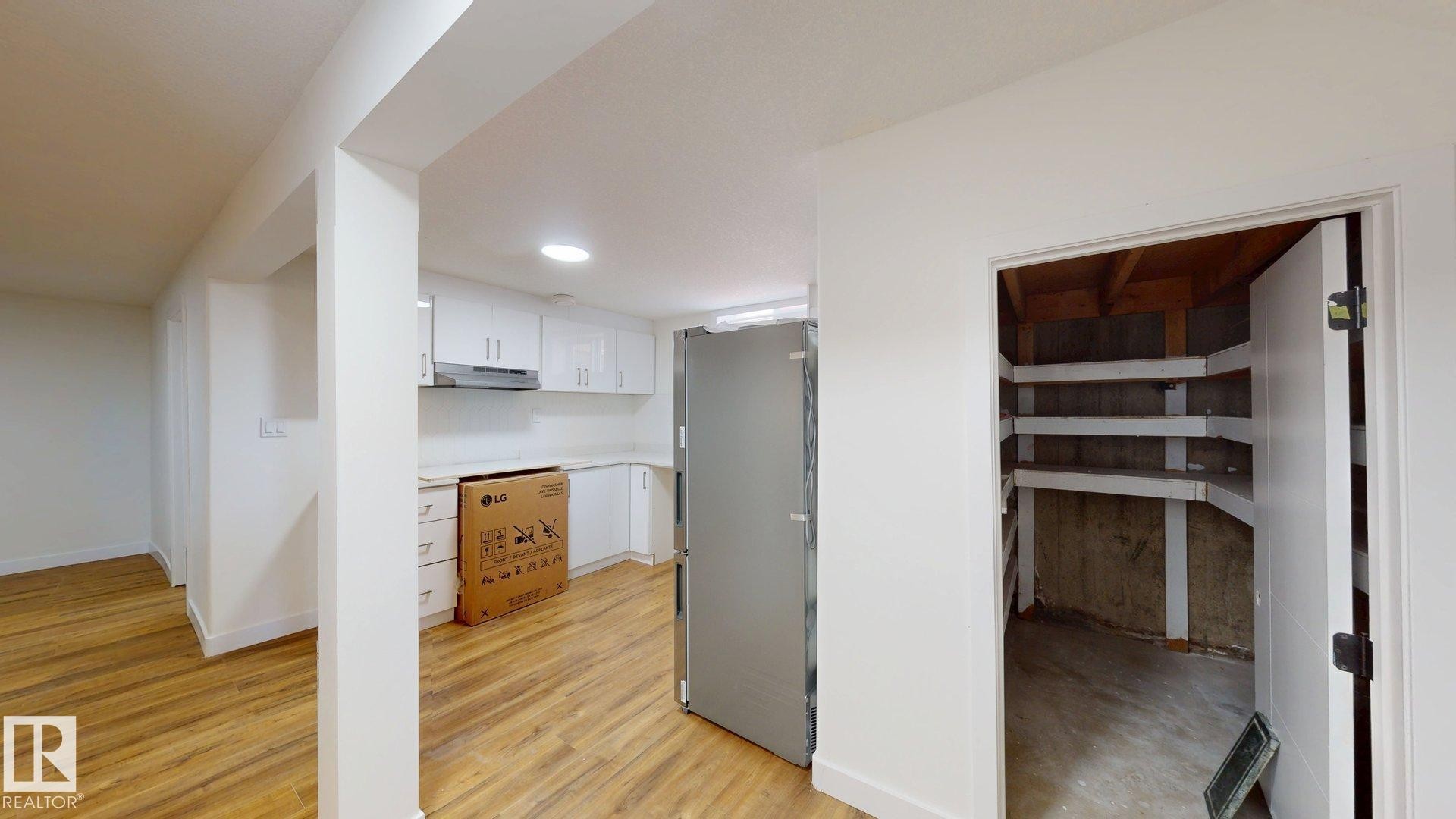 The kitchen area features white cabinetry, an exhaust hood, and wood-look flooring - 8515 86 Avenue, Edmonton, AB - Indoor