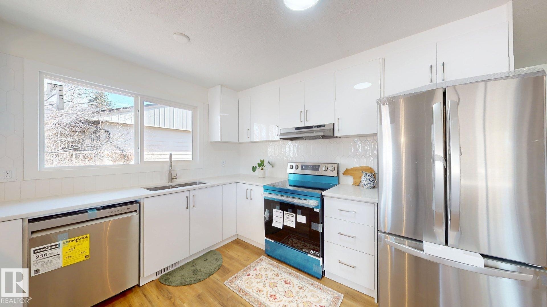 The kitchen features white cabinetry, stainless steel appliances, a white tile backsplash, and a window above the sink - 8515 86 Avenue, Edmonton, AB - Indoor Photo Showing Kitchen With Stainless Steel Kitchen With Double Sink