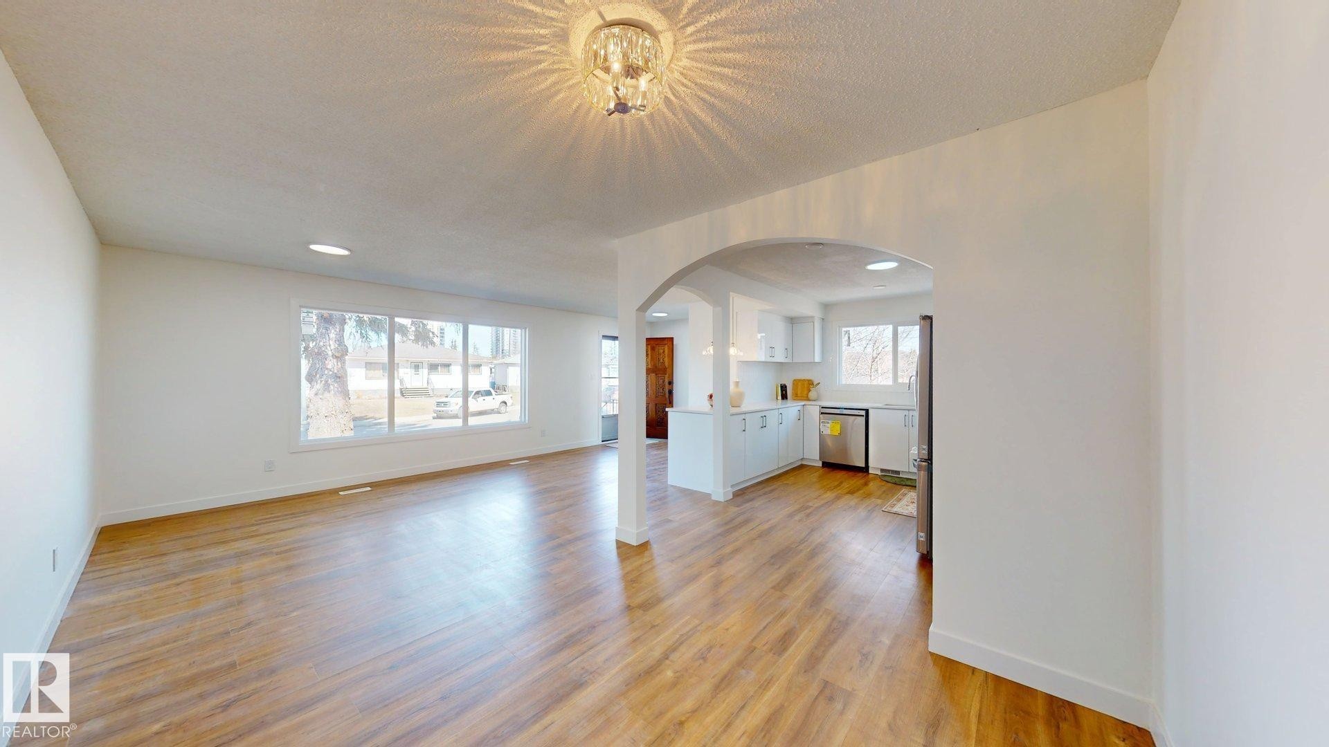 The expansive living area features wood-look flooring and a decorative ceiling light fixture - 8515 86 Avenue, Edmonton, AB - Indoor