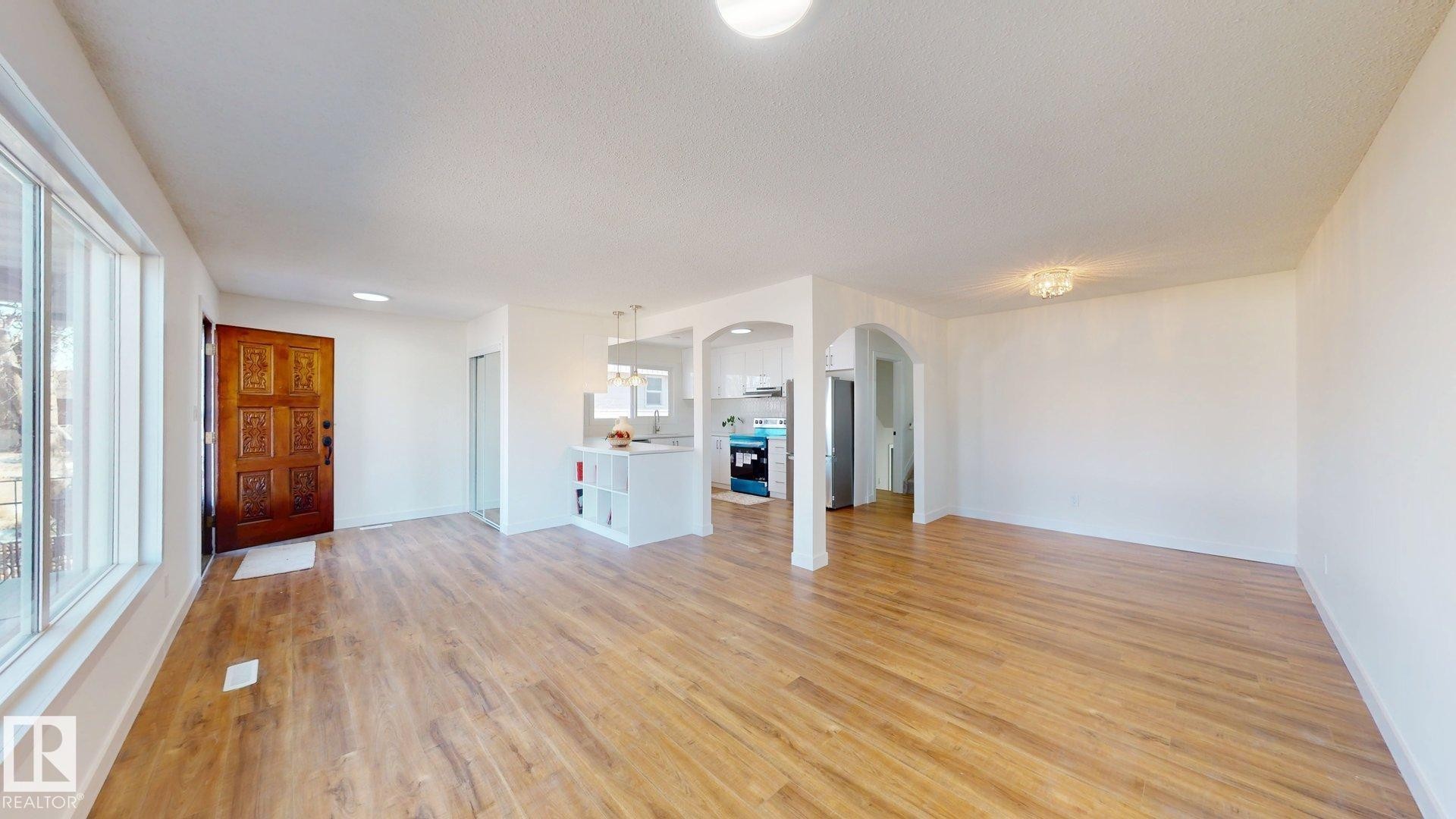 Spacious living area featuring hardwood flooring, white walls, and a decorative front entry door - 8515 86 Avenue, Edmonton, AB - Indoor Photo Showing Other Room