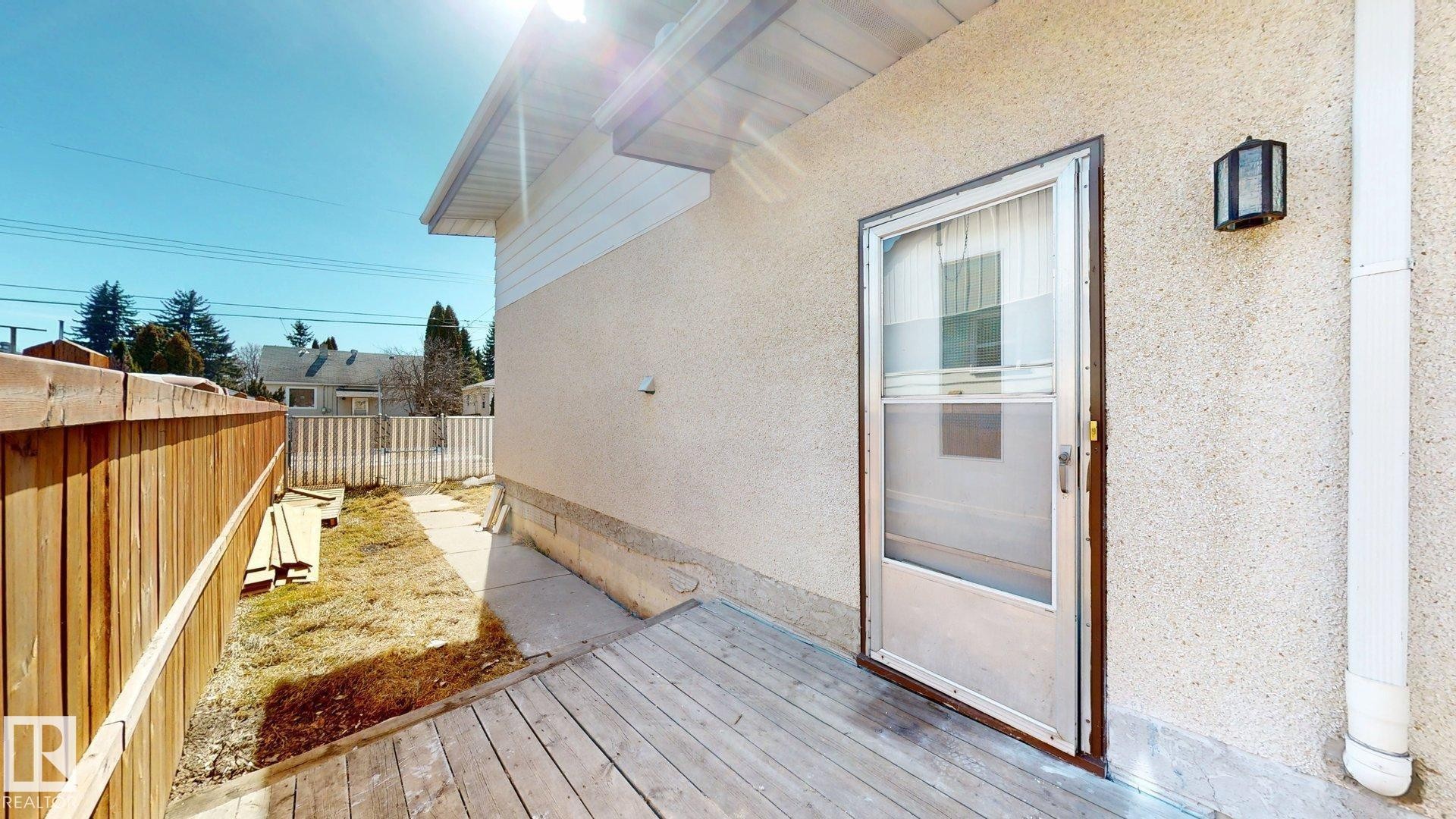 The property features an exterior deck area with a screen door entry, a light-colored stucco finish, and an outdoor wall sconce - 8515 86 Avenue, Edmonton, AB - Outdoor With Exterior