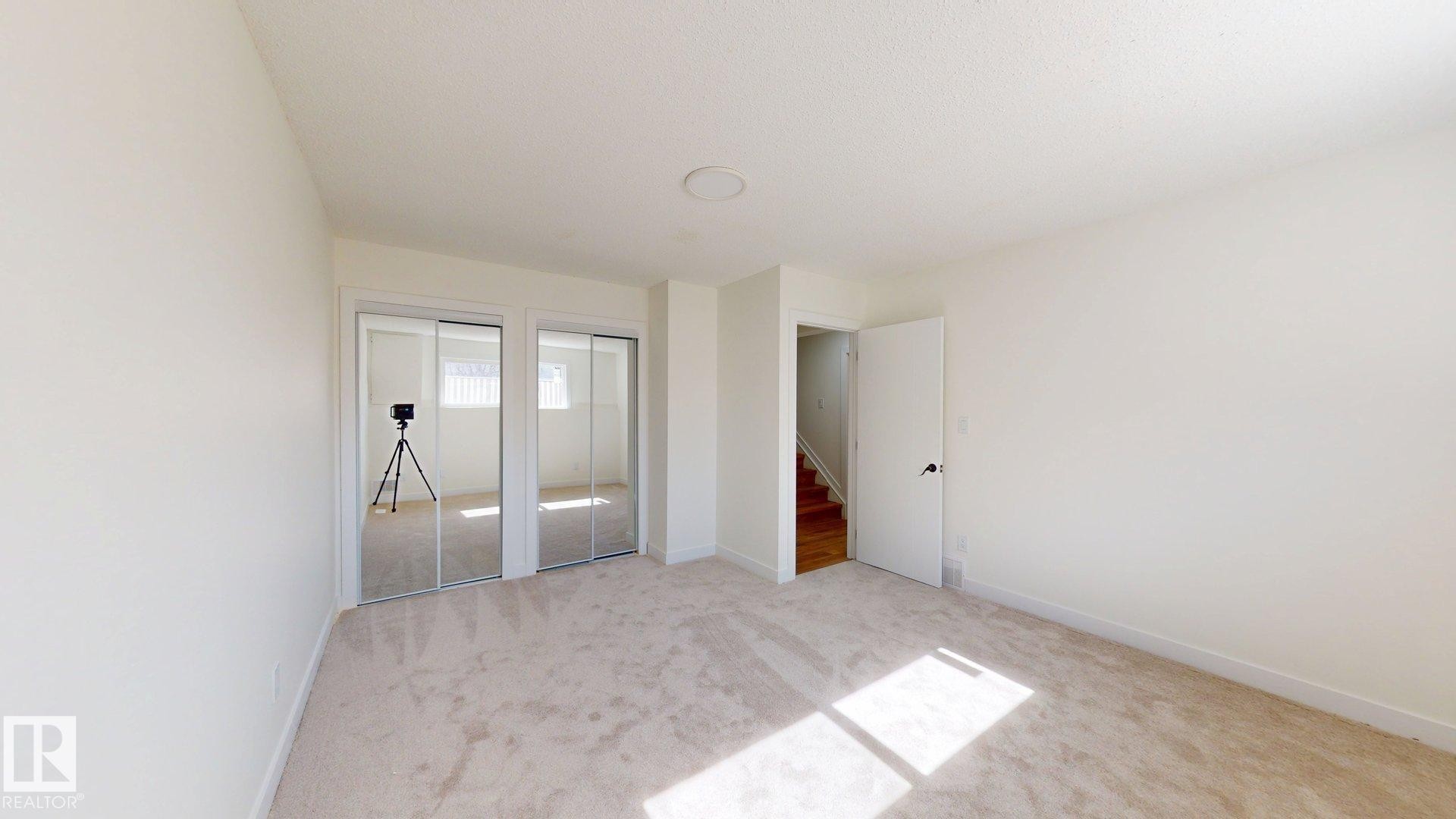 This room features light-colored carpeting, white walls, and a door leading to a wooden staircase - 8515 86 Avenue, Edmonton, AB - Indoor Photo Showing Other Room