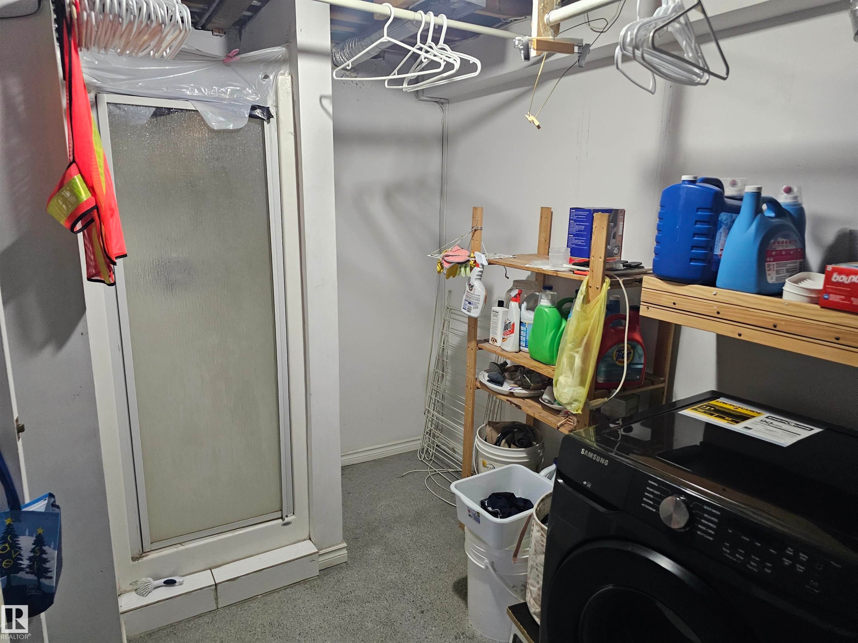 Utility room featuring a stand-alone shower enclosure, a black front-loading washing machine, and various wooden shelving units - 844 Erin Place, Edmonton, AB - Indoor