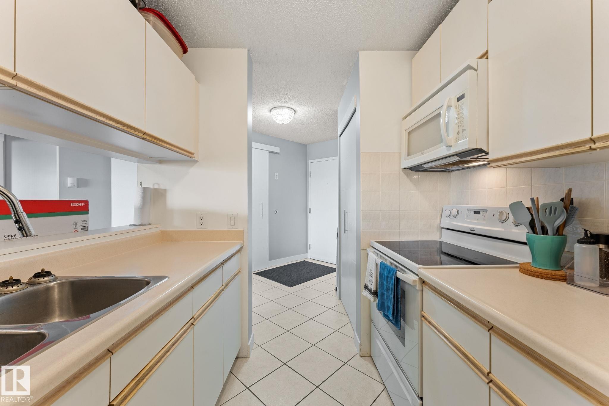 The kitchen features white cabinetry, light countertops, and a white tile floor - 208 6710 158 Avenue, Edmonton, AB
